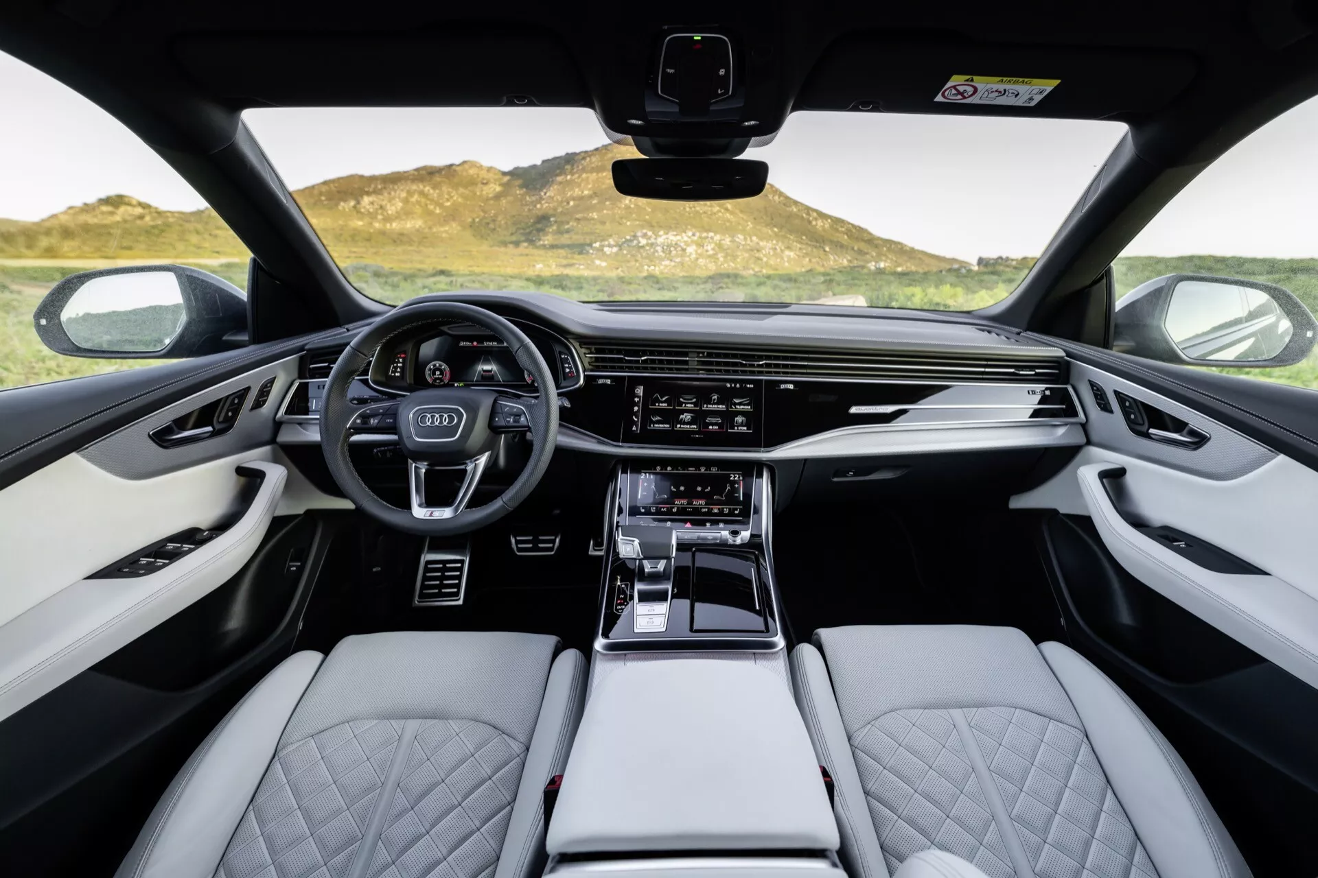 Interiér Audi Q8 2023 (4M-Facelift), pohľad do prednej kabíny z pohľadu prvej osoby so zameraním na športový multifunkčný volant, digitálny prístrojový panel, širokú dotykovú obrazovku infotainmentu, svetlé kožené sedadlá s prešívaným diamantovým vzorom a prvky z vysokej kvality materiálu.