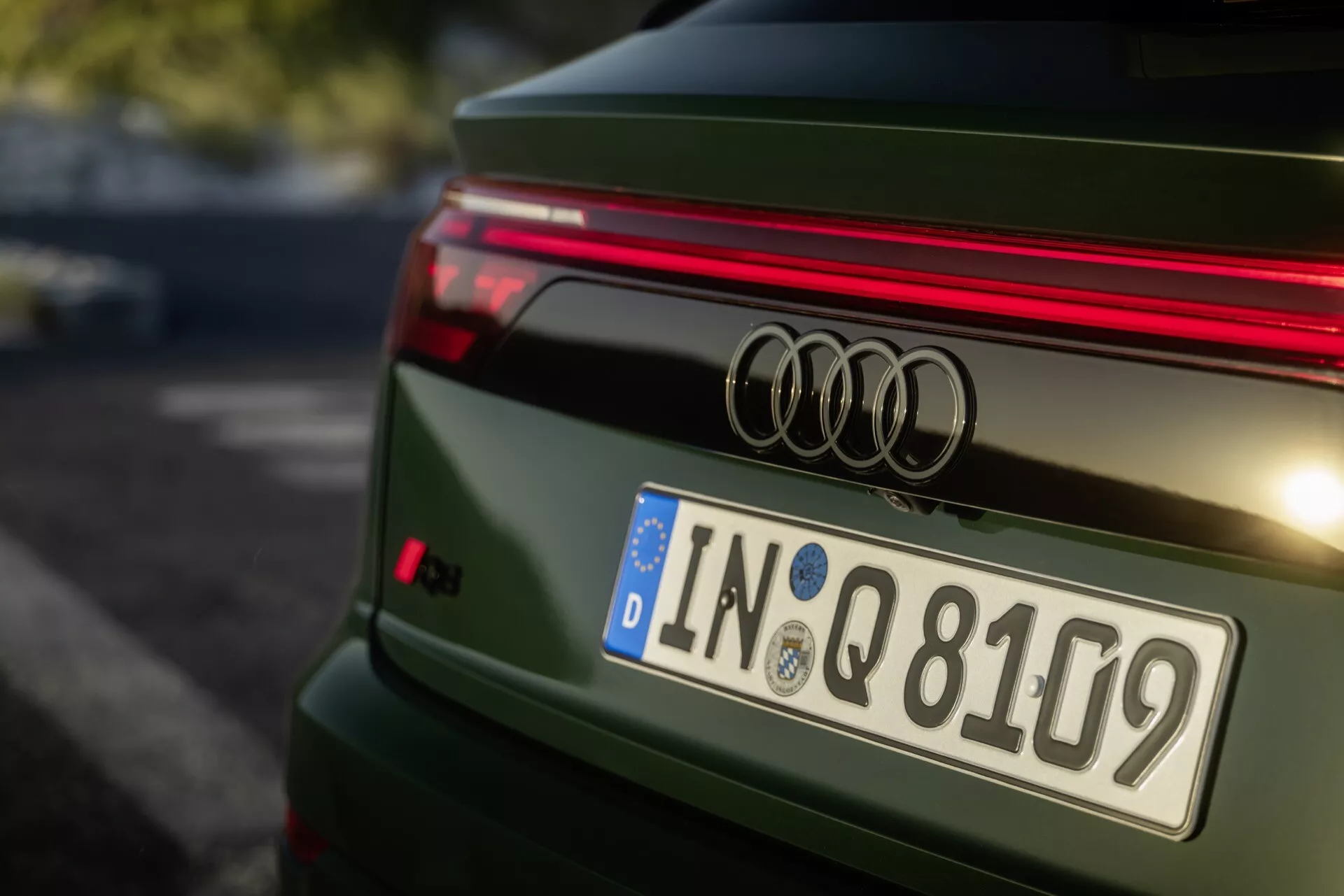 Detailný zadný pohľad na zelené Audi Q8 ročník 2023 po facelifte 4M, ukazujúci odznak Audi, horizontálny LED pás, európsku poznávaciu značku z Ingolstadtu a športový spojler na kufri s detailne navrhnutým a vylešteným kovovým povrchom.
