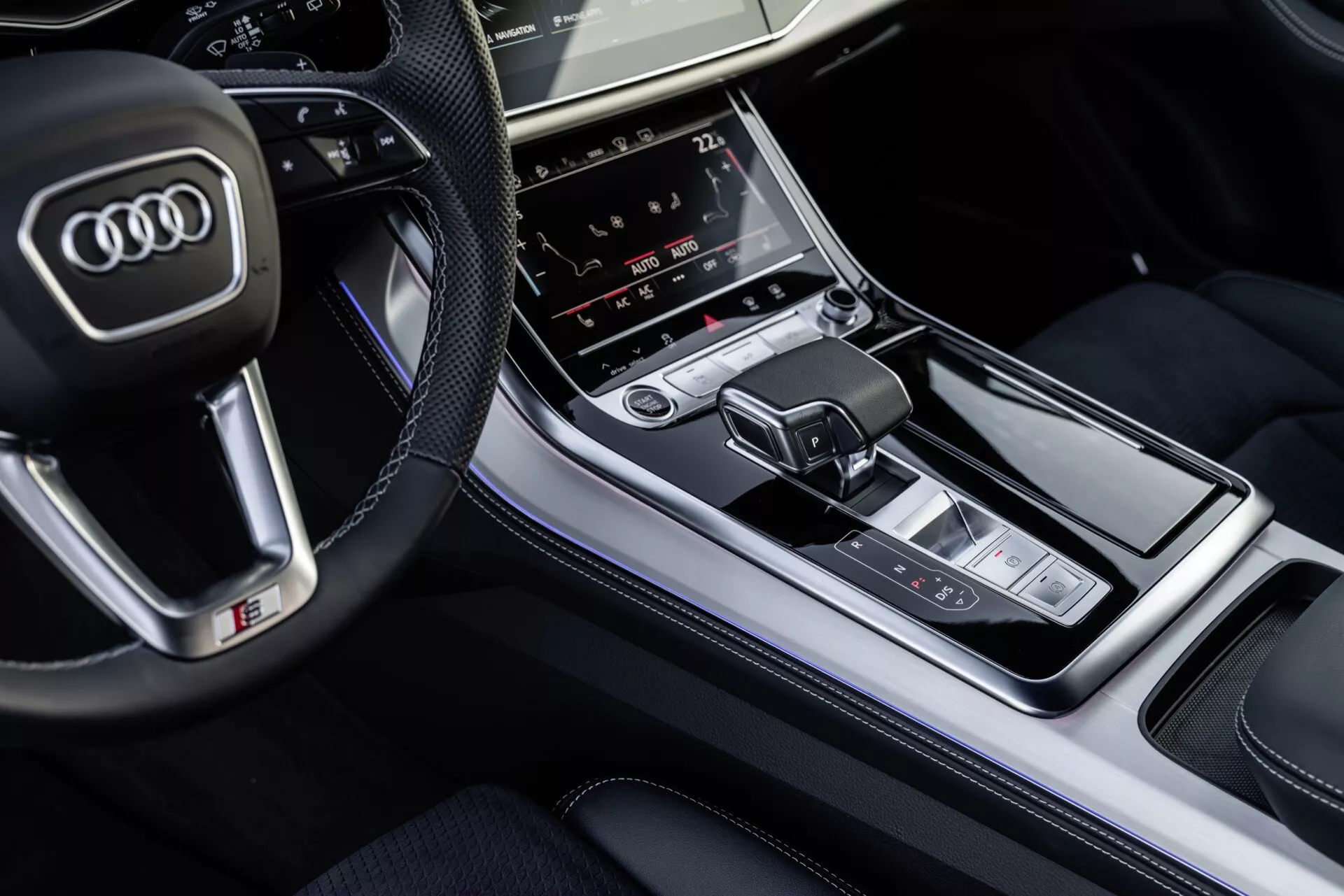 Pohľad zhora na interiér Audi Q8 2023 so zameraním na stredovú konzolu s radiacou pákou a panelom multimediálneho ovládania, zdôrazňujúci luxusné prevedenia a pokročilé technologické funkcie
