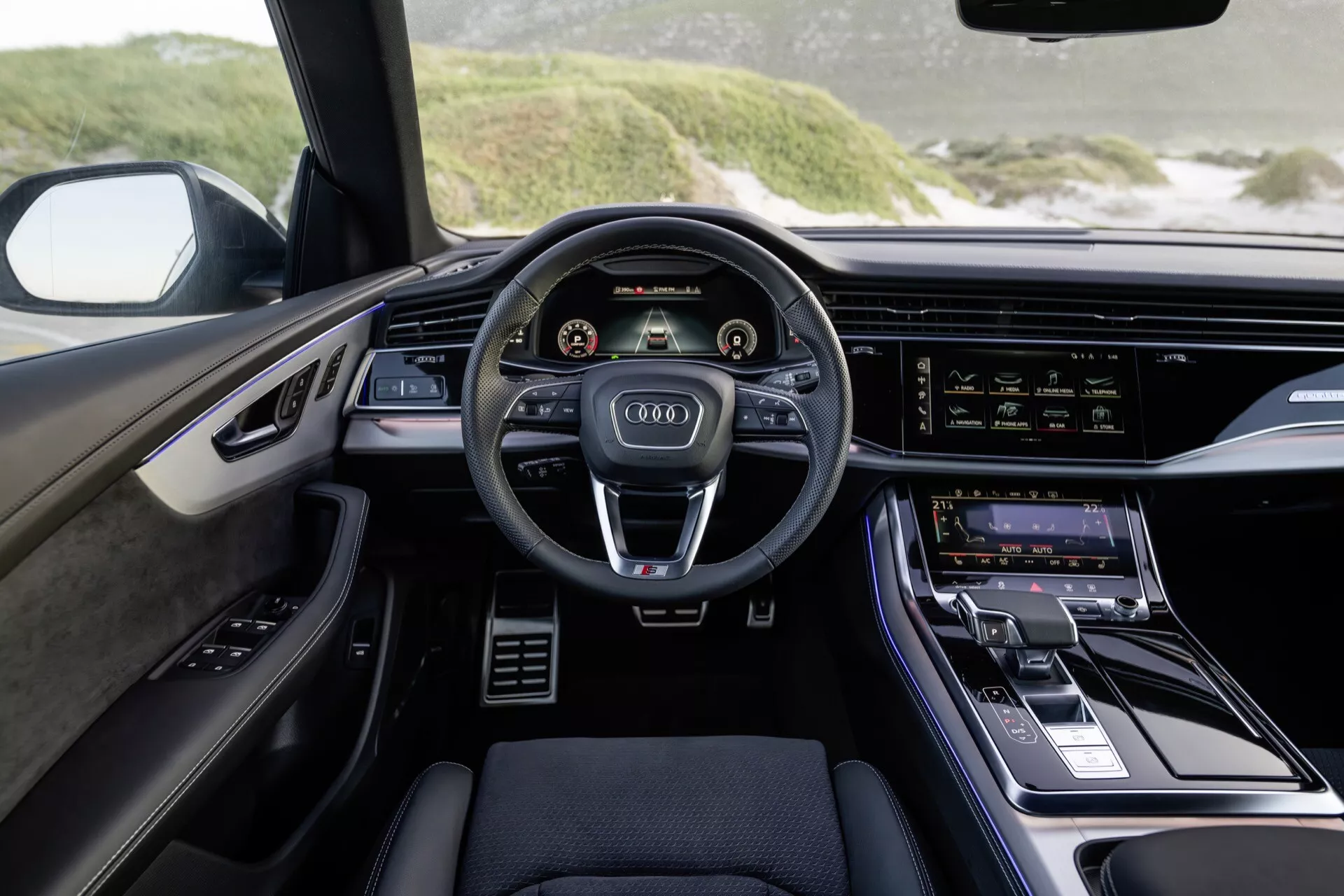 Interiér Audi Q8 2023 (4M-Facelift) z pohľadu vodiča zdôrazňujúci modernú palubnú dosku, volant s troma ramenami s ovládacími tlačidlami, dvojité digitálne displeje pre prístrojový panel a informačno-zábavný systém, a luxusné dizajnové akcenty.