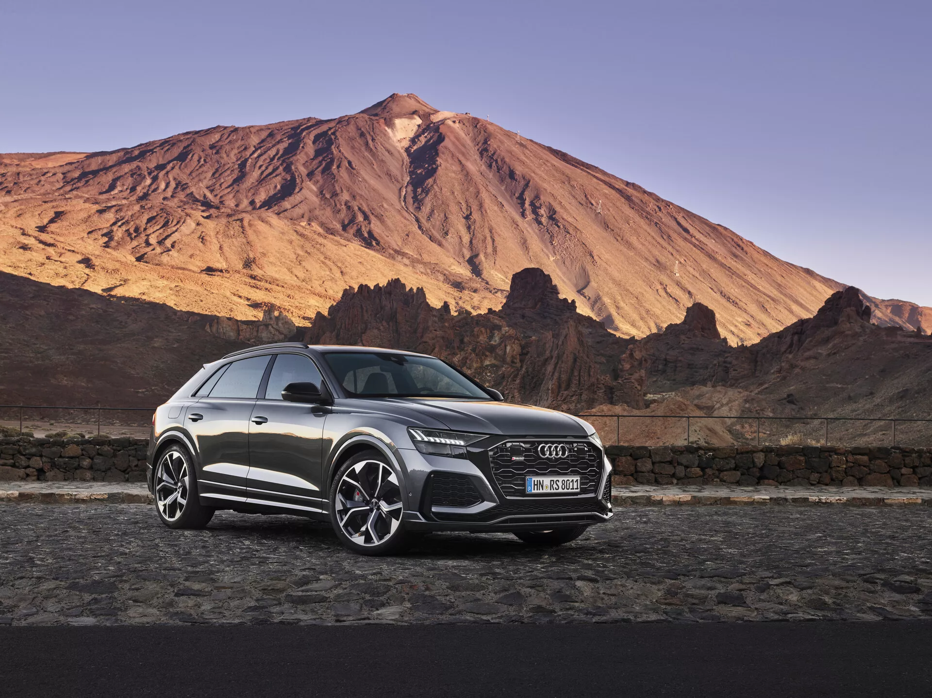 Luxusné SUV Audi Q8 2018 zaparkované pred dramatickým horským pozadím za úsvitu alebo súmraku pod jasnou oblohou, predstavujúce výraznú prednú mriežku, LED svetlomety, zliatinové kolesá a elegantné dizajnové prvky v mäkkom prirodzenom osvetlení.