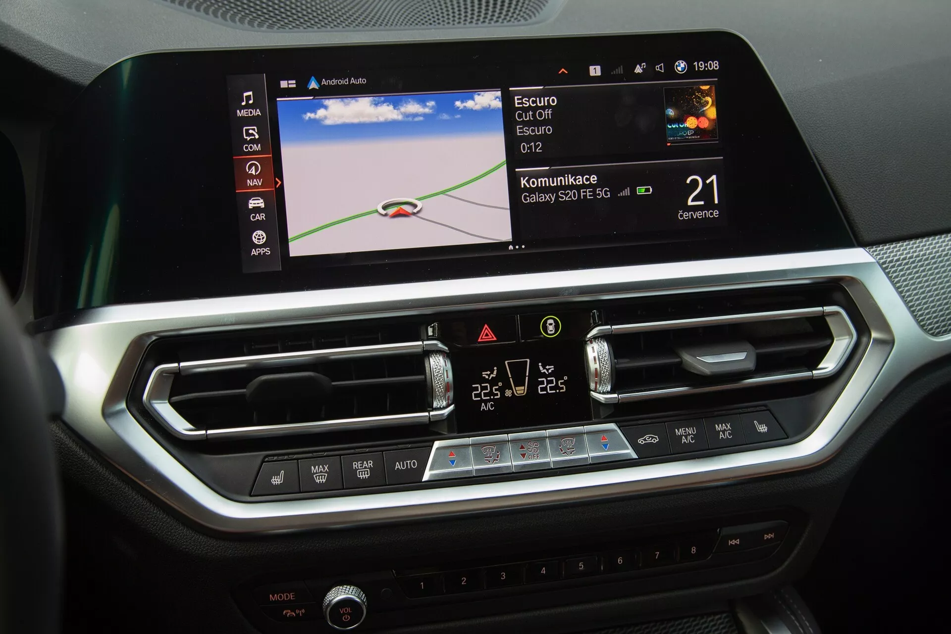 Centrálna konzola BMW 2-Series Coupe 2022 vyzdvihuje moderný infotainment systém a ovládanie klimatizácie automobilu. Obrázok zachytáva veľkú farebnú dotykovú obrazovku zobrazujúcu navigačnú mapu, ikony integrácie Bluetooth alebo smartfónu a hodiny. Pod obrazovkou sú dve stredové vzduchové výduchy s nastaviteľnými lamelami a elegantný panel s dotykovými tlačidlami a LCD displejom pre dvojzónovú klimatizáciu. Dizajn interiéru s brúsenými kovovými akcentmi a textúrami pripomínajúcimi uhlíkové vlákna odráža luxusné a technologicky orientované prostredie.