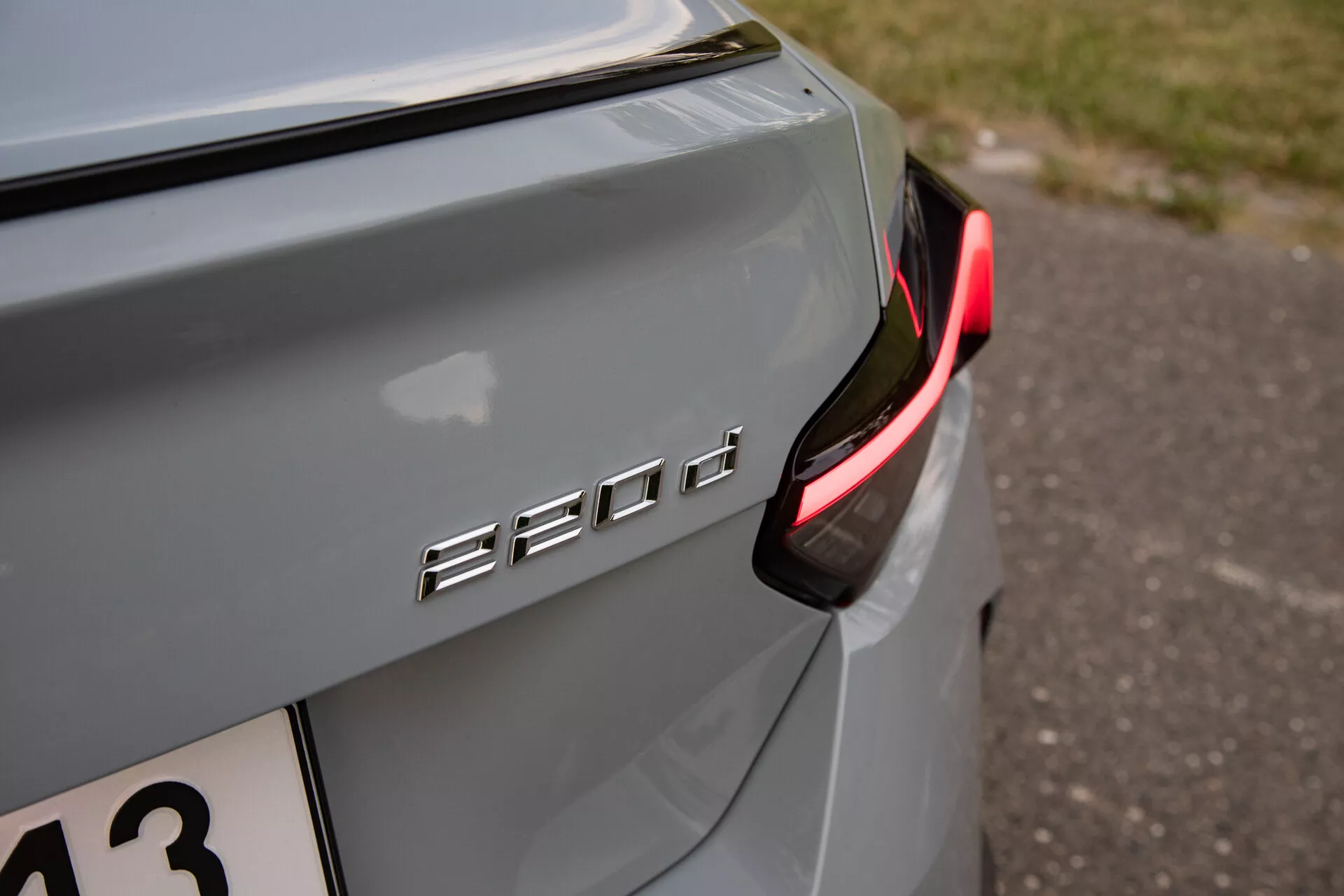 Detailný záber na zadnú pravú časť BMW 530d, zvýrazňujúci označenie modelu '530d' a zameriavajúci sa na moderné, čiastočne osvetlené zadné LED svetlo. Farba auta je metalická strieborná alebo sivá s jemným odrazom v prirodzenom svetle, čo naznačuje večerné alebo tieňové prostredie. Značka je chrómová alebo kovová, kontrastujúca s farbou auta a umiestnená na veku kufra. Predstavuje malú hĺbku ostrosti, ktorá zdôrazňuje značku '530d' a blízku časť karosérie, zatiaľ čo pozadie je rozmazané, vhodné pre milovníkov automobilovej technológie alebo dizajnu vozidiel.