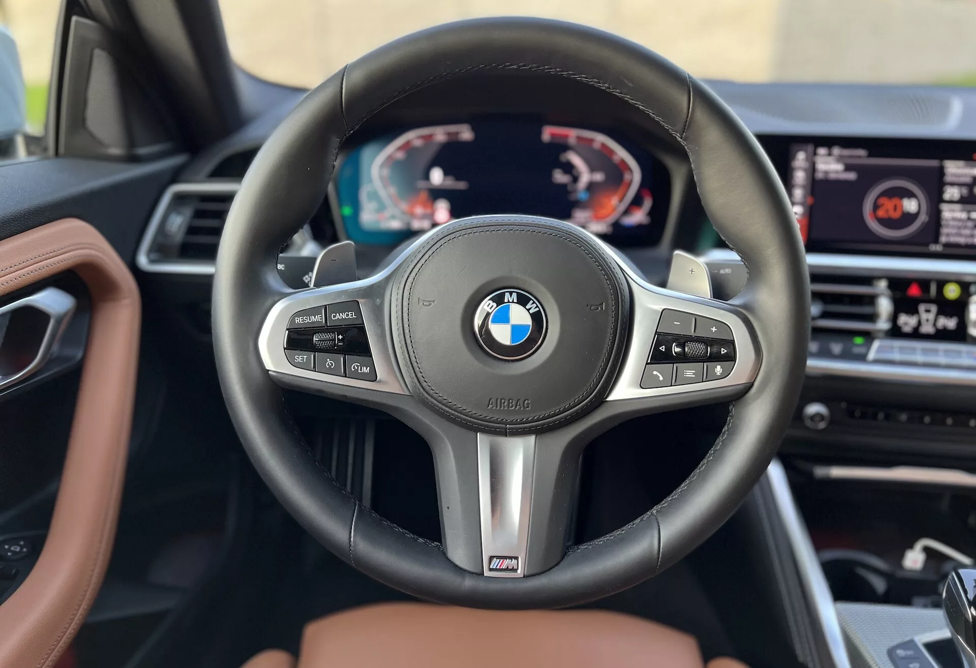 Vnútorný záber vozidla BMW 2er-Reihe 2022 zameraný na volant a prístrojovú dosku z pohľadu vodiča. Obsahuje trojramenný volant BMW s multifunkčnými tlačidlami na tempomat, správu audia a telefonovanie, spolu s radiacimi pádlami a odznakom výkonu 'M'. Za volantom je digitálny prístrojový panel zobrazujúci otáčkomer, rýchlomer a multifunkčné informácie. Infotainment systém je viditeľný v strede prístrojovej dosky a vnútorná výbava zahŕňa kožu a drevo, čo naznačuje prémiový model.