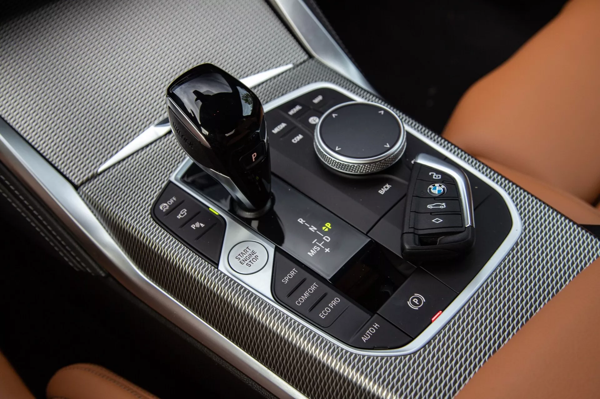 Detailný záber na stredovú konzolu BMW 2er-Reihe 2022, zvýrazňujúci radiacu páku, ovládací otočný volič multimediálneho systému a dotykový ovládací panel s lesklým čiernym a karbónovým povrchom.