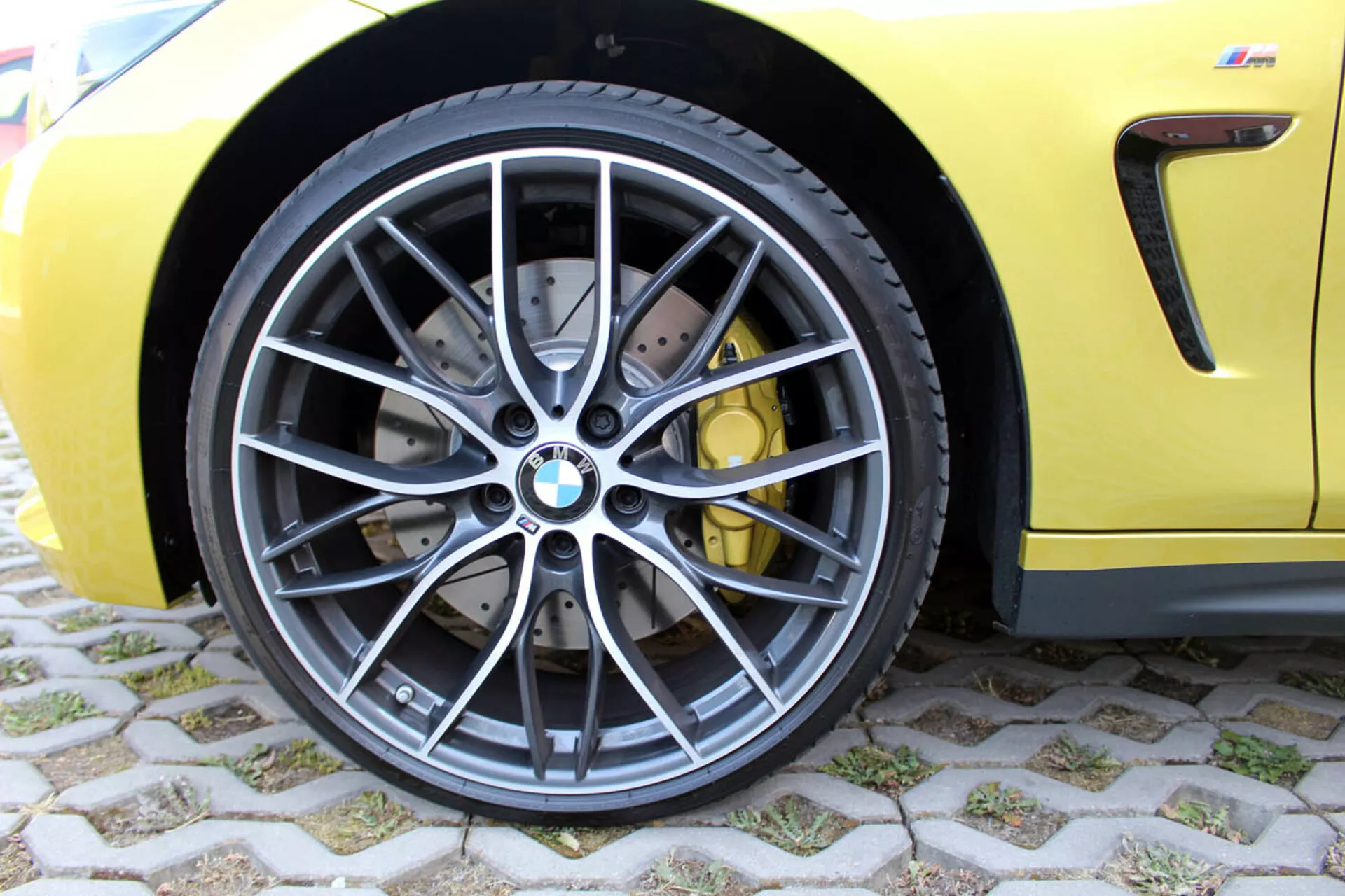 Detailný pohľad na predné koleso BMW 4 Series Coupe 2013 s dizajnom z tmavosivej zliatiny s viacerými paprskami, nízkoprofilovou radiálnou bezdušovou pneumatikou, vysoko výkonným brzdovým systémom s prederavovanými kotúčmi a žltými strmienmi, na pozadí športovo žltej karosérie