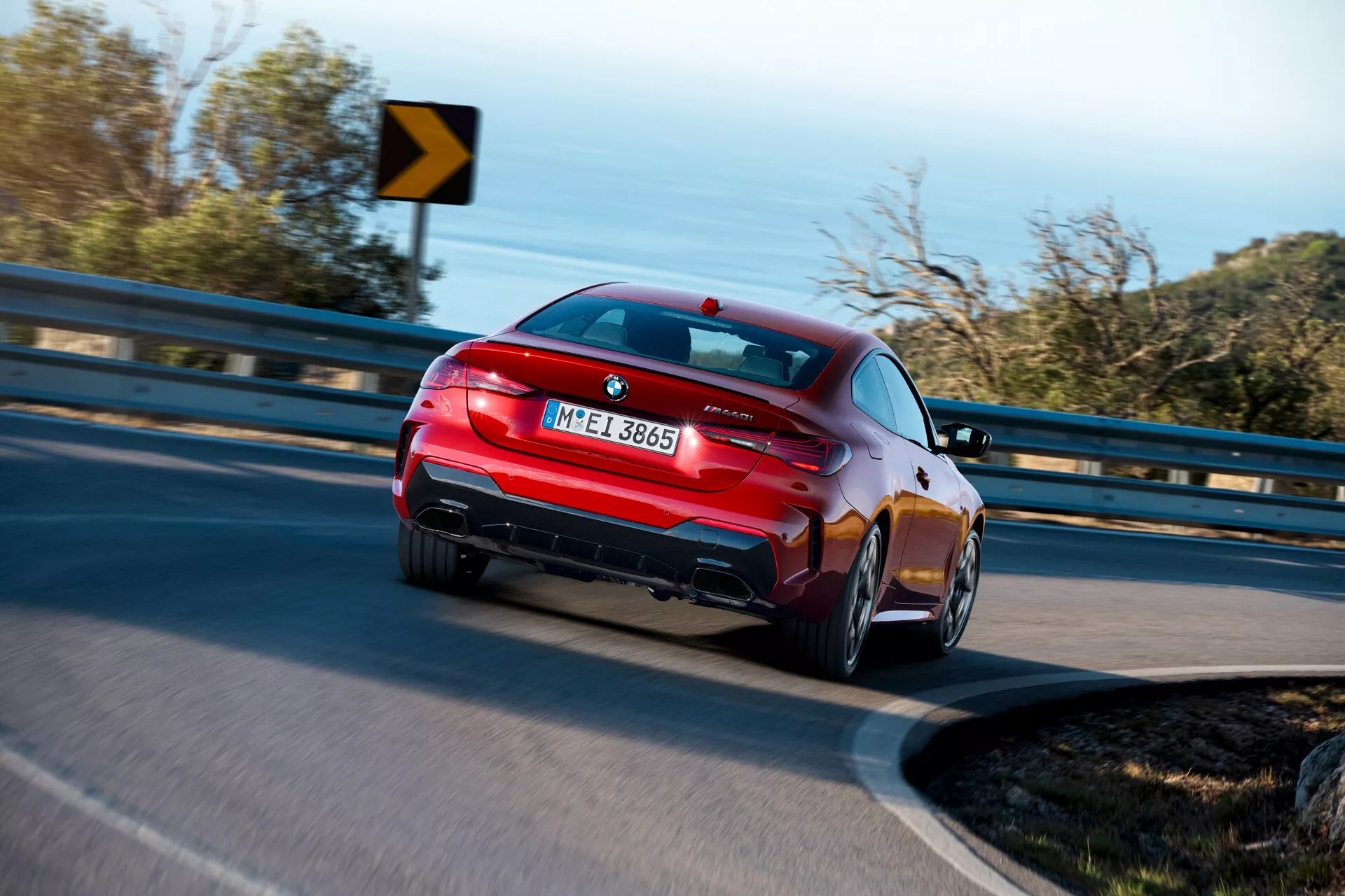 Coupe BMW radu 4 (G22-G23-G26-G82-G83 facelift) rok 2024 zobrazené z uhla tri štvrtiny zozadu, prezentujúce jeho športový dizajn, úzke vodorovné zadné svetlá, dvojité výfukové koncovky, integrovaný zadný spojler, kolesá s viacramenným dizajnom a lesklý lak v pohybe na zákrute