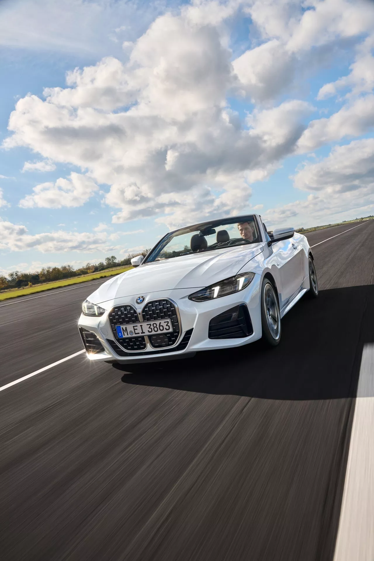 BMW radu 4 kabriolet (G22-G23-G26-G82-G83 Facelift) ročník 2024 v bielej farbe, idúce po suchej asfaltovej ceste pod čiastočne zamračenou oblohou, ukazujúce dynamický pohľad z troch štvrtín