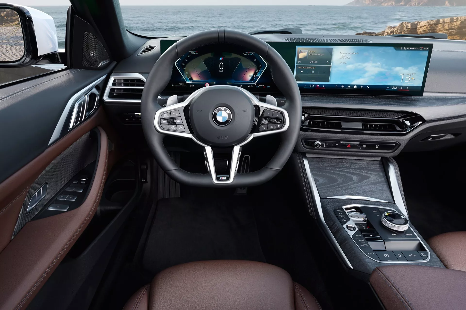 Interiérový pohľad na BMW radu 4 2024 (G22-G23-G26-G82-G83-facelift) z pohľadu vodiča s trojramenným volantom obaleným v koži, úplne digitálnym prístrojovým panelom, pokročilou multimediálnou centrálnou konzolou s dotykovým displejom, luxusnými koženými sedadlami v hnedej farbe s drevodekorom a modernými ergonomickými prvky vrátane multifunkčných ovládaní a digitálneho palubného dosky