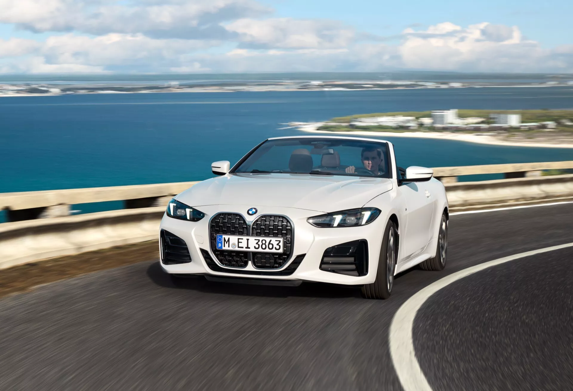 BMW radu 4 kabriolet 2024 (facelift G22-G23-G26-G82-G83) v pohybe na pobrežnej ceste so zloženou strechou, s LED svetlometmi, dvojitou obličkovou mriežkou a športovými zliatinovými kolesami