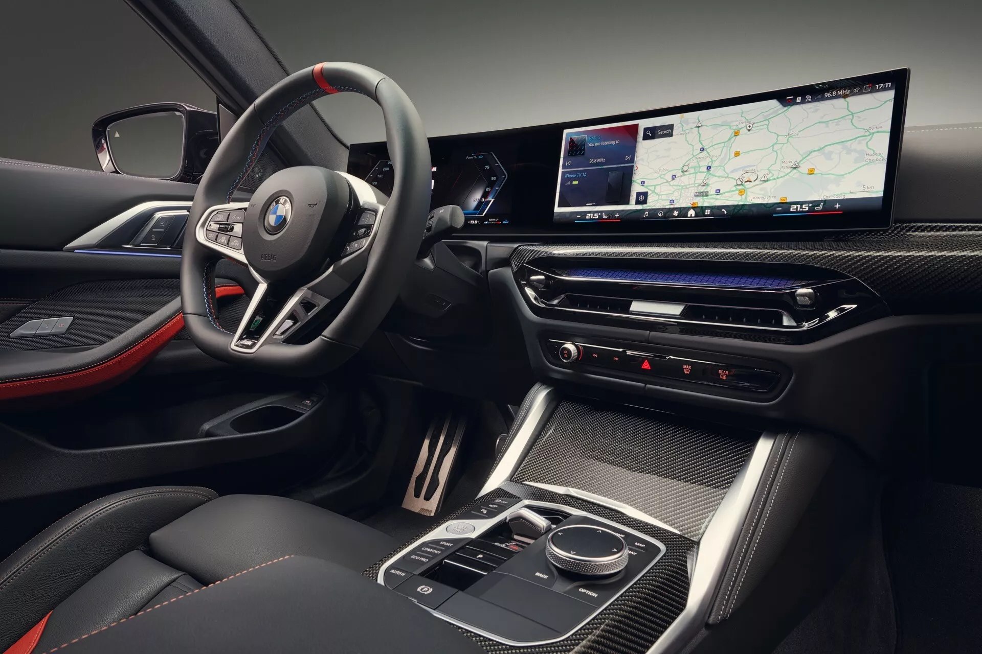 Pohľad do interiéru BMW radu 4 ročník 2024 (G22-G23-G26-G82-G83 Facelift) ukazujúci odznak na športovom, multifunkčnom volante, digitálny palubný počítač s dlhým displejom, štýlovú stredovú konzolu s vysokým leskom a sedadlá s dvojfarebnou farebnou schémou s červenými prvkami.