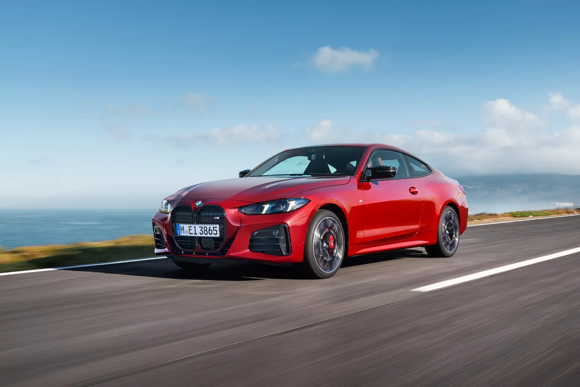 Žiarivo červené kupé BMW radu 4 z roku 2024 (G22-G23-G26-G82-G83-Facelift) so športovým postojom na pobrežnej ceste ukazujúce aerodynamický dizajn, elegantné LED svetlomety a charakteristickú masku