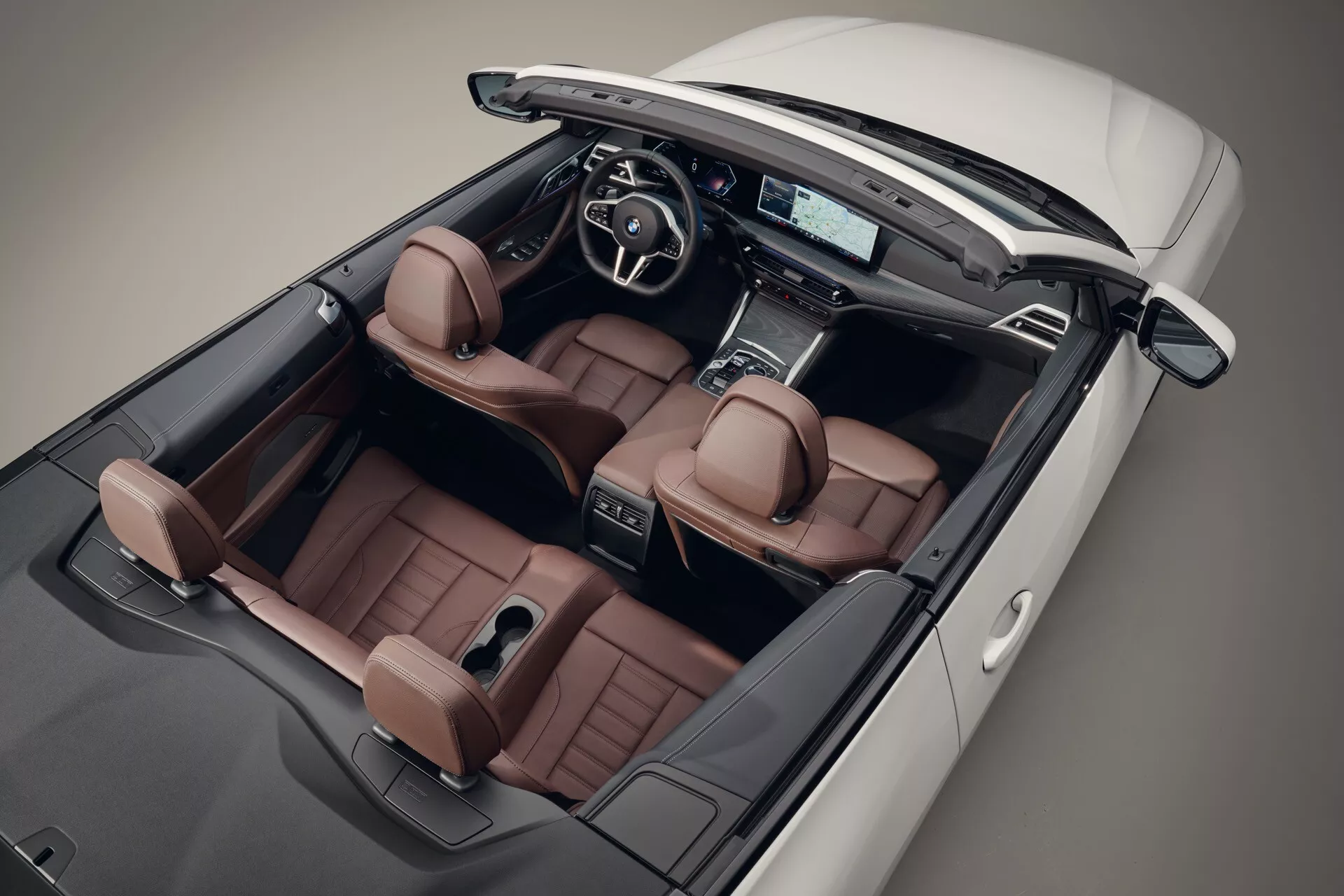 Pohľad z vtáčej perspektívy na kabriolet BMW radu 4 z roku 2024 so zloženou strechou, ktorý zobrazuje luxusné sedadlá z kože v teplej hnedej farbe, modernú prístrojovú dosku s pokročilou obrazovkou infotainmentu a športový multifunkčný volant