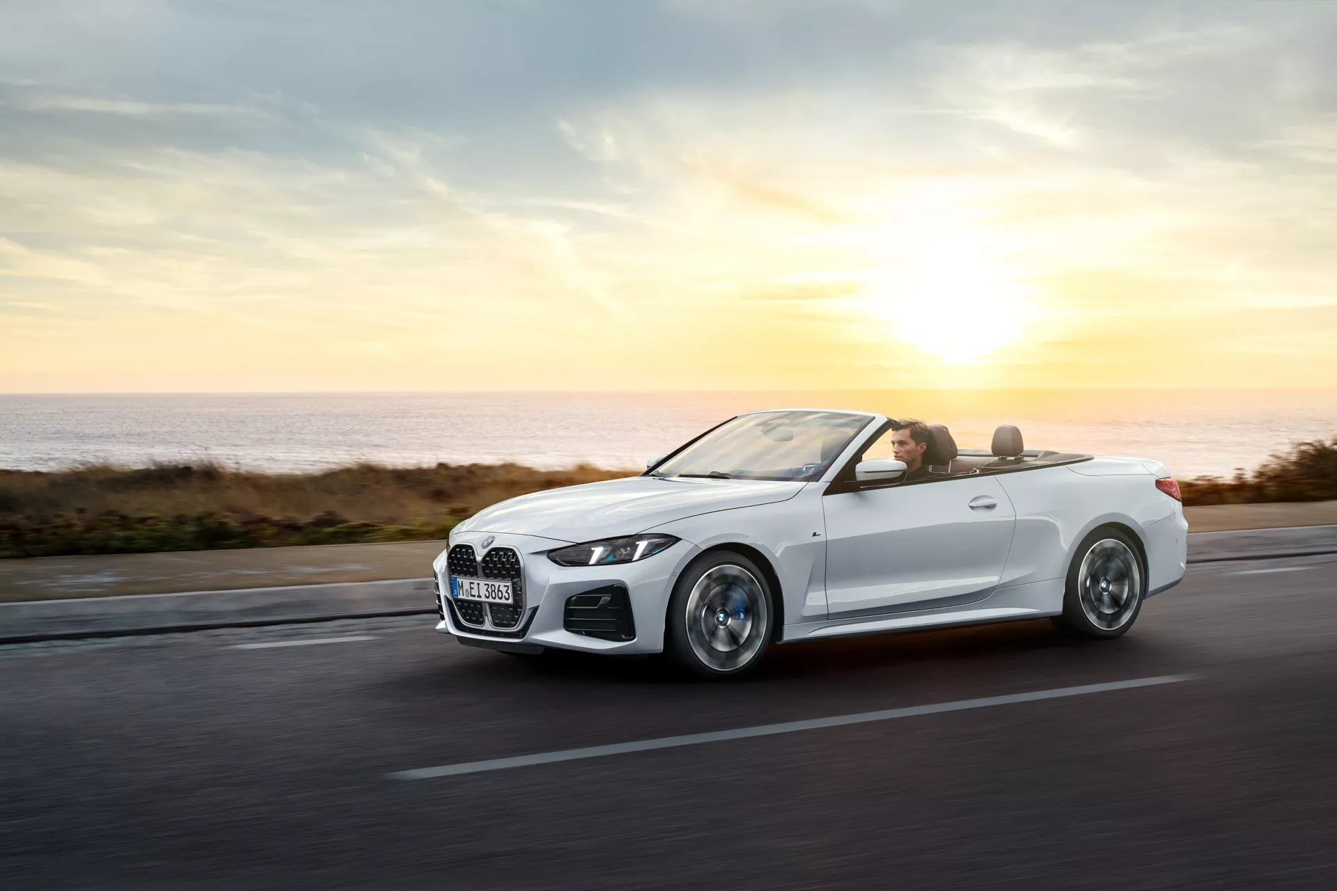 BMW radu 4 kabriolet (G22-G23-G26-G82-G83 Facelift) z roku 2024 v pohybe na pobrežnej ceste pri východe alebo západe slnka, predvádzajúce svoje aerodynamické karosérie, zliatinové kolesá, LED svetlomety, luxusný interiér a pokročilé technológie