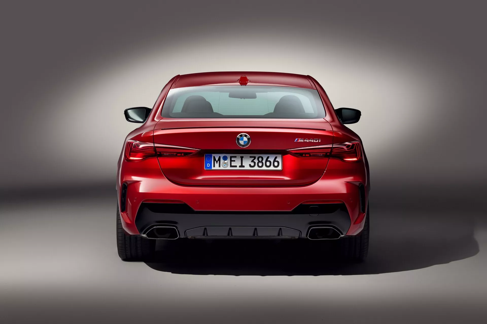 Zadný pohľad na červené BMW M5 zobrazujúce L-tvarované zadné svetlá, emblém, odznak modelu M5 a dvojité výfukové rúry s difúzorom, štúdiová snímka s profesionálnym osvetlením