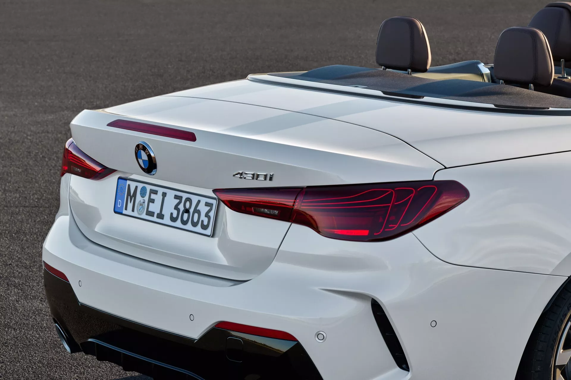 Zadný pohľad na biely kabriolet BMW radu 4 (facelift 2024) s LED svetlami v tvare L, dvojitými výfukmi a športovým difúzorom, ktorý jasne zameriava na jeho aerodynamickú zadnú siluetu a technologické funkcie ako sú zadné parkovacie senzory