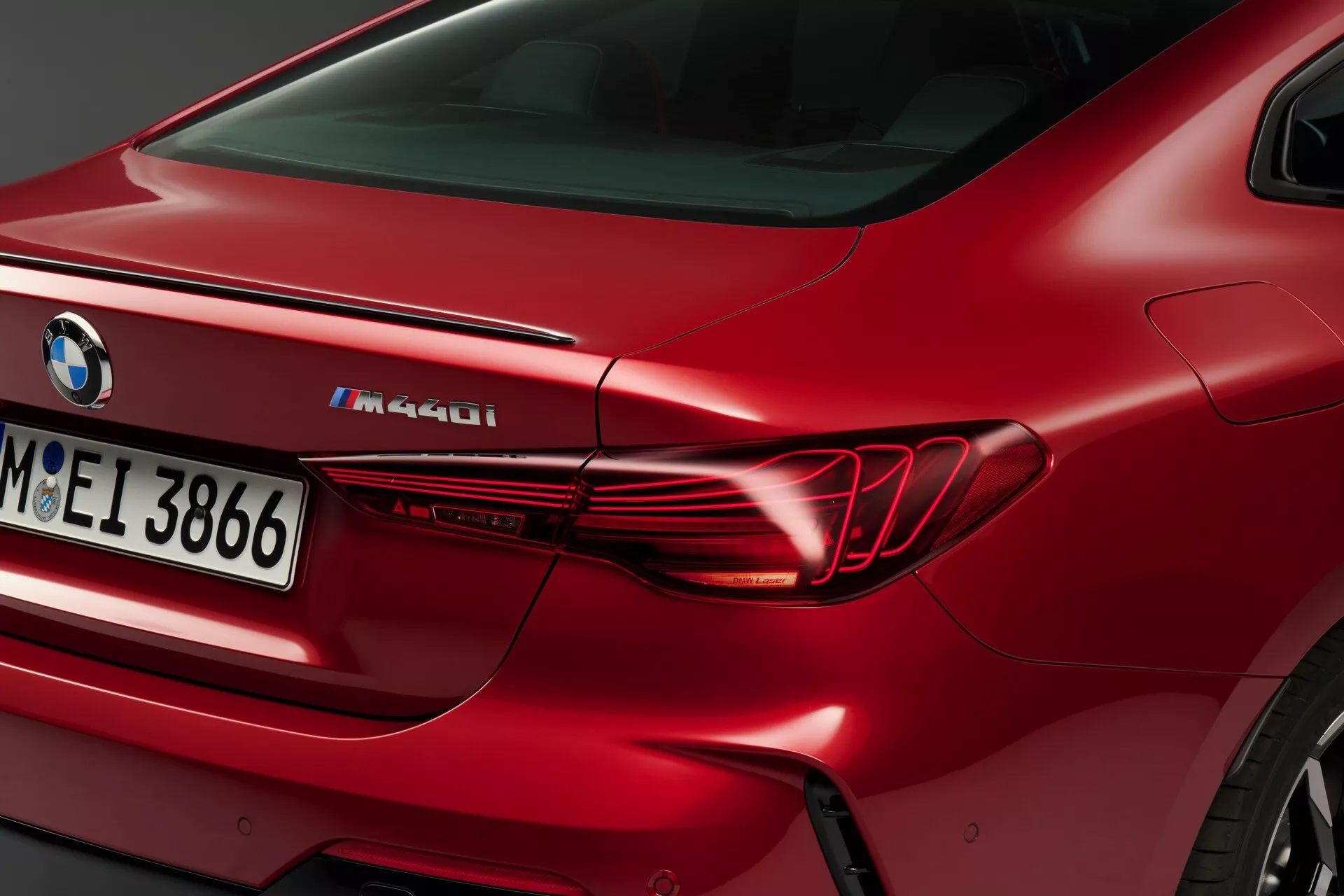 Detailný pohľad na zadnú štvrtinu červeného BMW M440i 2024, vrátane elegantného horizontálneho dizajnu zadných svetiel, tvarovaného zadného blatníka a označenia M Performance na veku batožinového priestoru.
