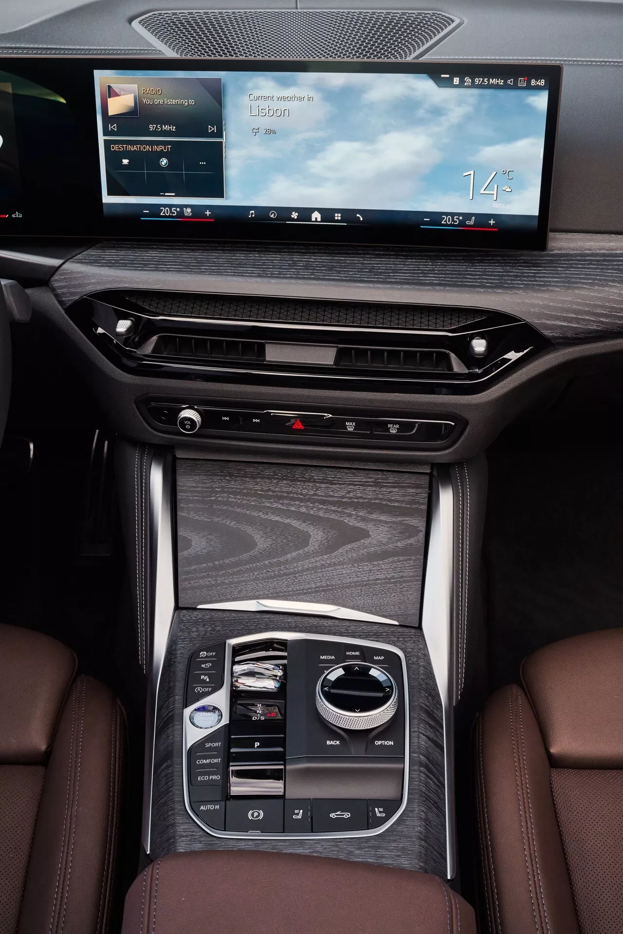 Pohľad zvrchu nadol na stredovú konzolu BMW radu 4 2024 (G22-G23-G26-G82-G83 facelift) zvýrazňujúci obrazovku infotainmentu, otvory klimatizácie, vysoko lesklú dýhu a moderný elektrický radenie v interiéri luxusného vozidla