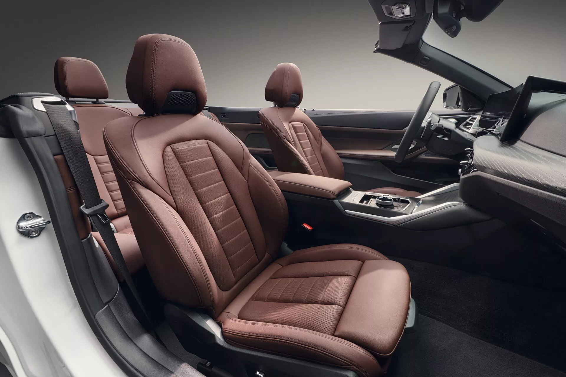 Interiérový pohľad na BMW radu 4 z roku 2024 (G22-G23-G26-G82-G83 facelift) z vyvýšenej perspektívy ukazujúci luxusné hnedé kožené sedadlá so zložitým šitím, pokročilé ovládacie prvky na stredovej konzole a priestranný dizajn kabíny, ktorý zdôrazňuje sofistikované spracovanie a moderné technologické vybavenie.