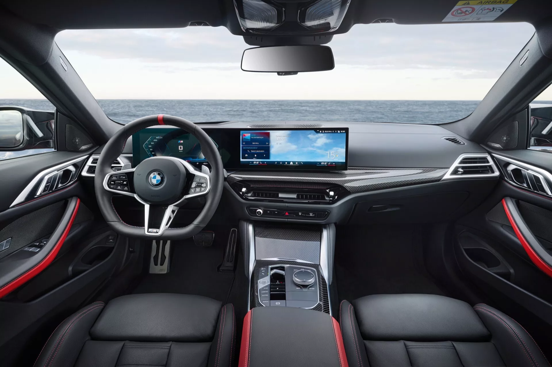Interiérový pohľad na BMW radu 4 z roku 2024 (G22-G23-G26-G82-G83 facelift) ukazujúci športový palubný panel, multifunkčný volant s pádlami na radenie, digitálny prístrojový panel a širokouhlý informačný systém vo vysokom rozlíšení z pohľadu zo zadného sedadla