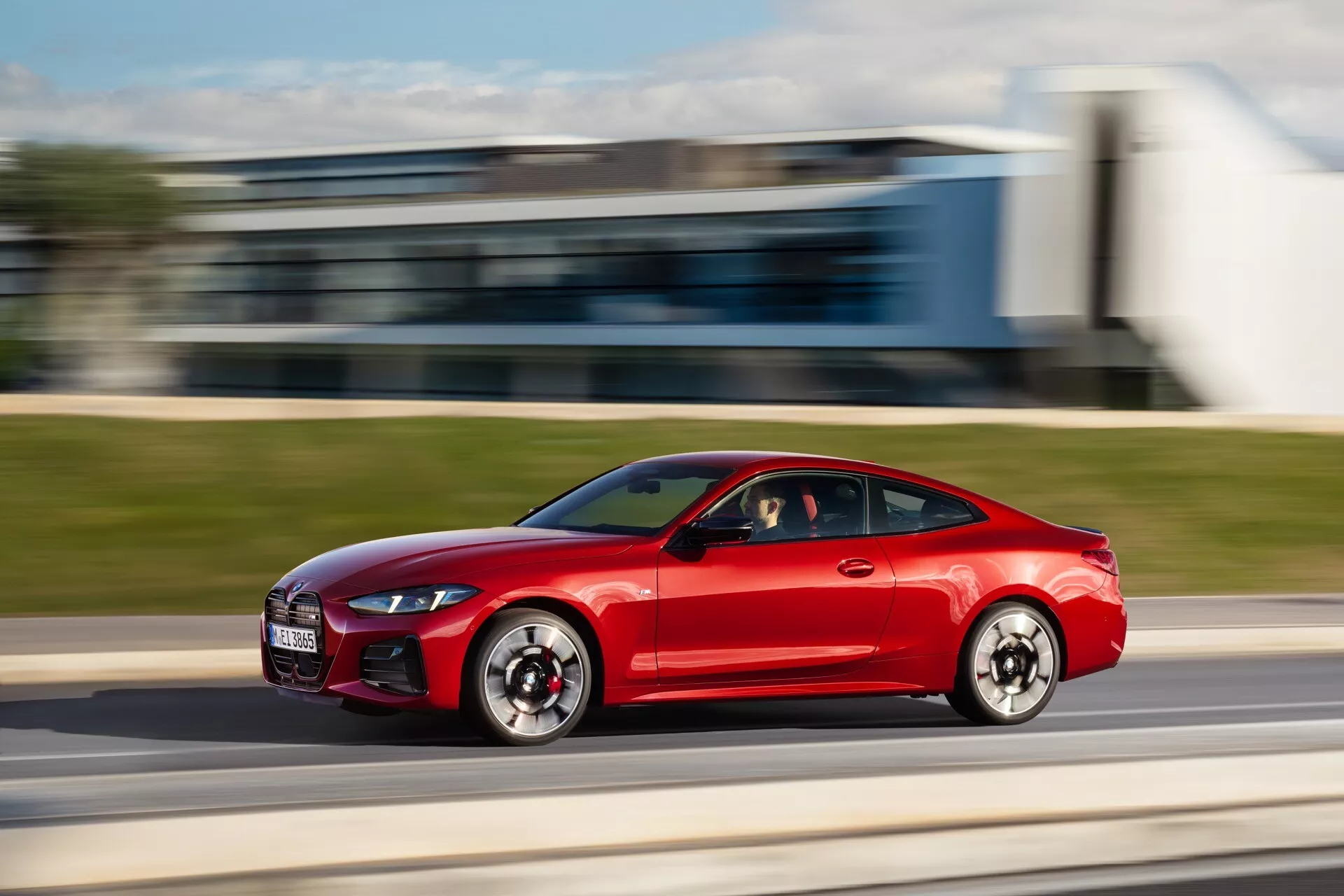 Červené športové kupé BMW radu 4 (G22-G23-G26-G82-G83 Facelift) v pohybe, bočný pohľad s technikou panorámovania zobrazujúca aerodynamický dizajn, LED denné svetlá a na výkon orientované veľké vzduchové vstupy.