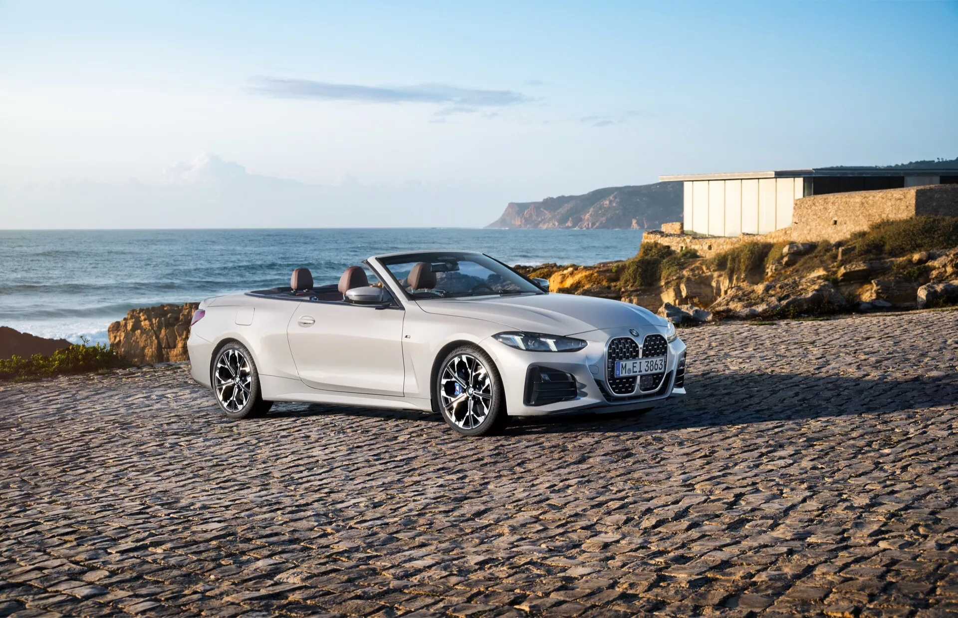 BMW radu 4 kabriolet (G22-G23-G26-G82-G83 Facelift) ročník 2024 zaparkované na dlažobných kameňoch v pobrežnom prostredí, ukazuje ľavú prednú stranu, LED svetlomety, veľkú mriežkovú mriežku a štýlové zliatinové kolesá pod teplým svetlom neskorého popoludnia