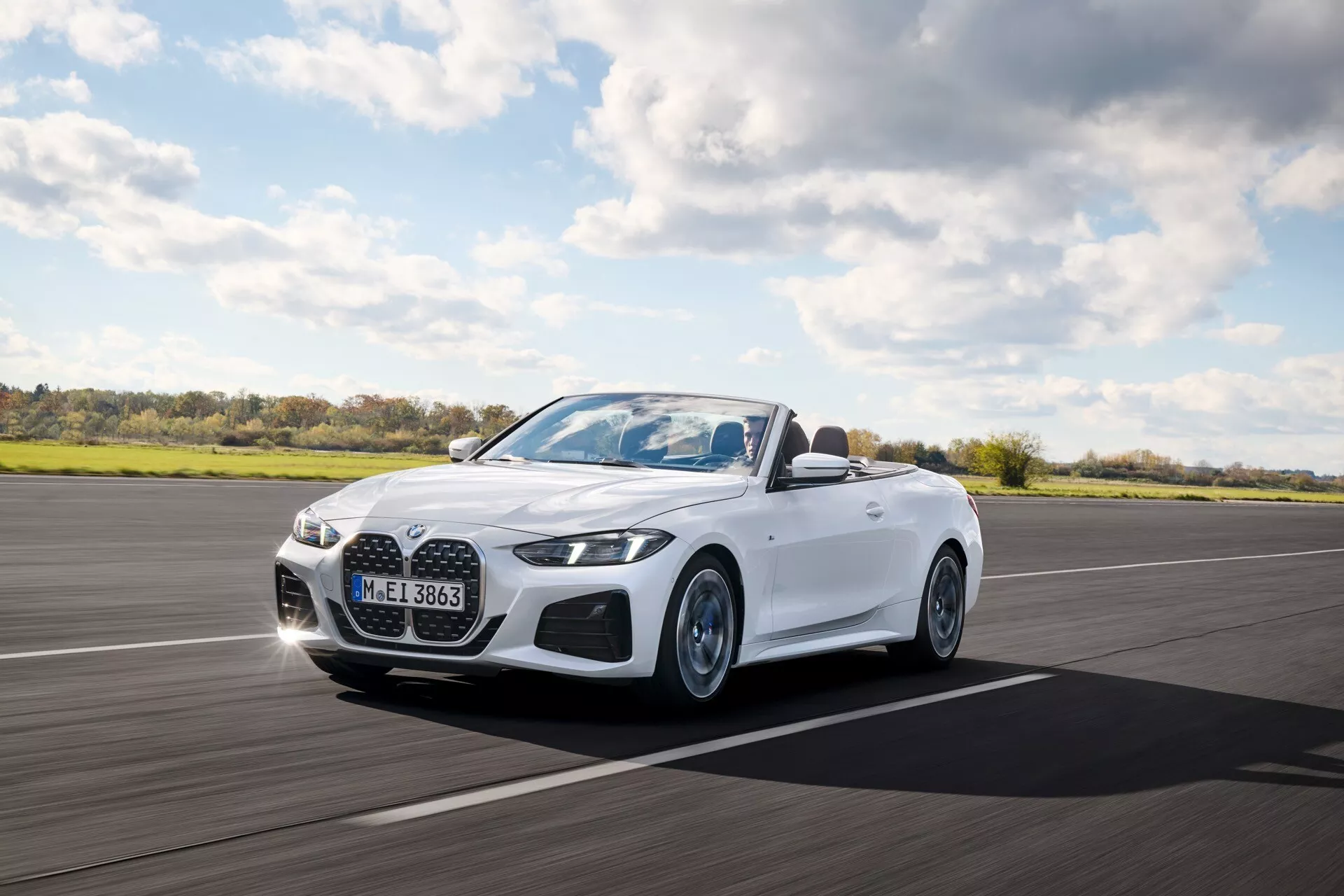 BMW radu 4 kabriolet (G22-G23-G26-G82-G83 Facelift) 2024 v pohybe, zobrazujúce LED svetlomety, výraznú mriežku chladiča a biely exteriér z pohľadu trojštvrte z prednej časti