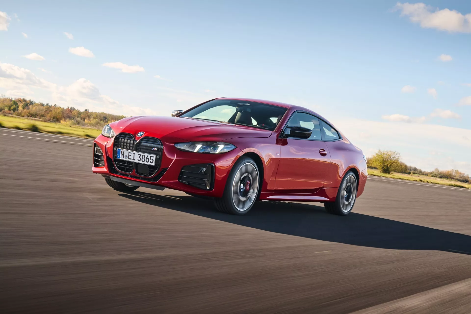 Dynamický pohľad na červené športové kupé BMW rady 4 (G22-G23-G26-G82-G83 Facelift) v pohybe, zvýrazňujúci elegantné línie karosérie, charakteristickú prednú mriežku, športový nárazník so vzduchovými vstupmi a prvky zamerané na výkon, zachytené pod uhlom 45 stupňov zvýrazňujúce aerodynamický profil.