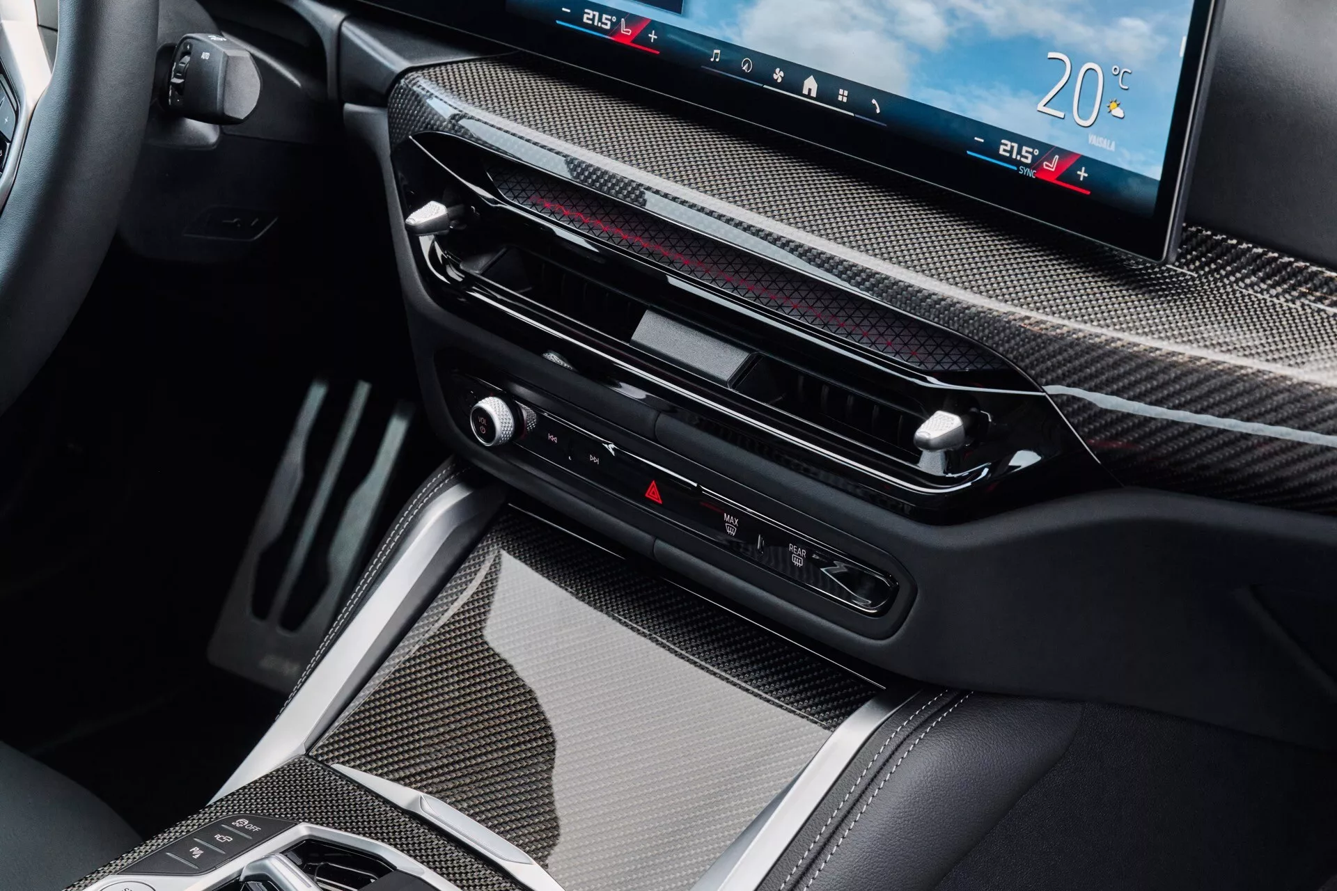 Detailný interiérový pohľad na model BMW radu 4 pre rok 2024, ktorý predstavuje priestor stredovej konzoly s obkladom z uhlíkových vlákien, veľký digitálny displej pre informačno-zábavný systém a ovládanie klímy, tenké výduchy vzduchu, dotykové tlačidlá vrátane ovládania výstražných svetiel a modernú elektronickú radicu páku, symbolizujúcu pokročilú prevodovú technológiu a luxus.