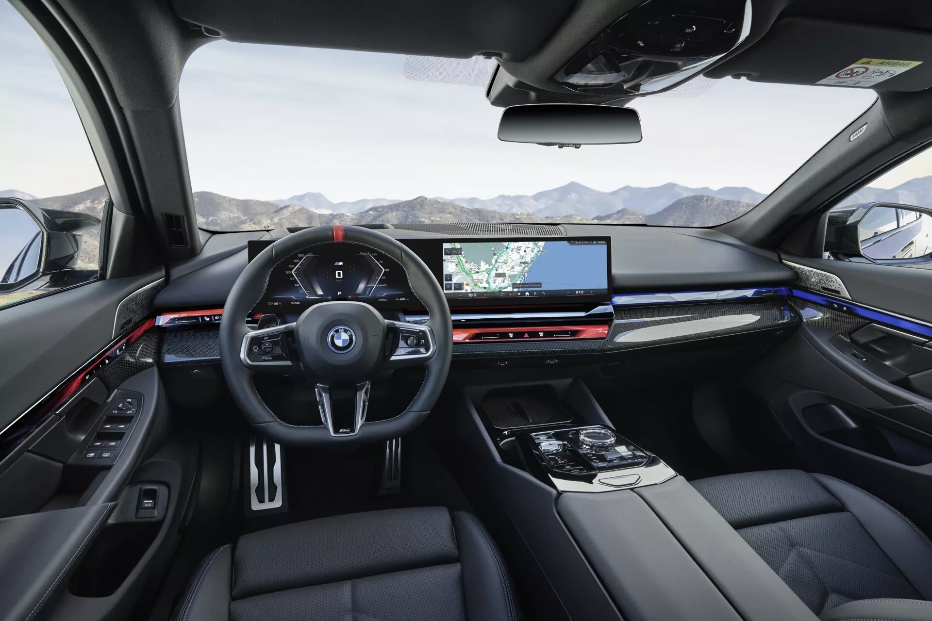 Interiér BMW radu 5 (G60-G61) 2023 z pohľadu zadných sedadiel na digitálny prístrojový panel a širokouhlý displej infotainment s navigáciou, ovládaním klímy, luxusným čalúnením a panoramatickou strechou