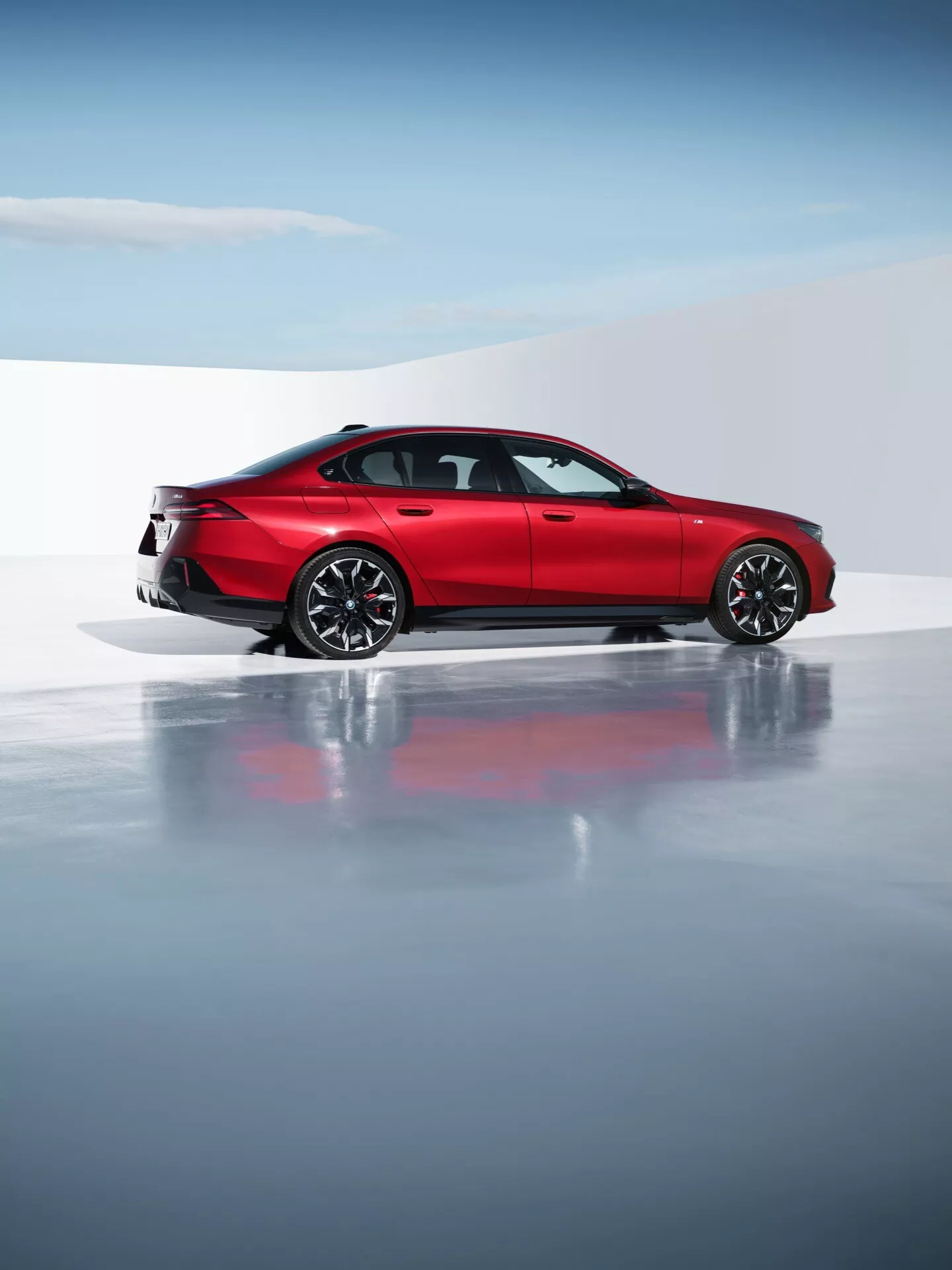 BMW radu 5 (G60-G61) 2023 vo výraznej červenej farbe predstavujúci jeho aerodynamický dizajn a športovú eleganciu, s viacerými zliatinovými kolesami, modernými LED zadnými svetlami a dvojitým výfukovým systémom v profesionálnom štúdiu