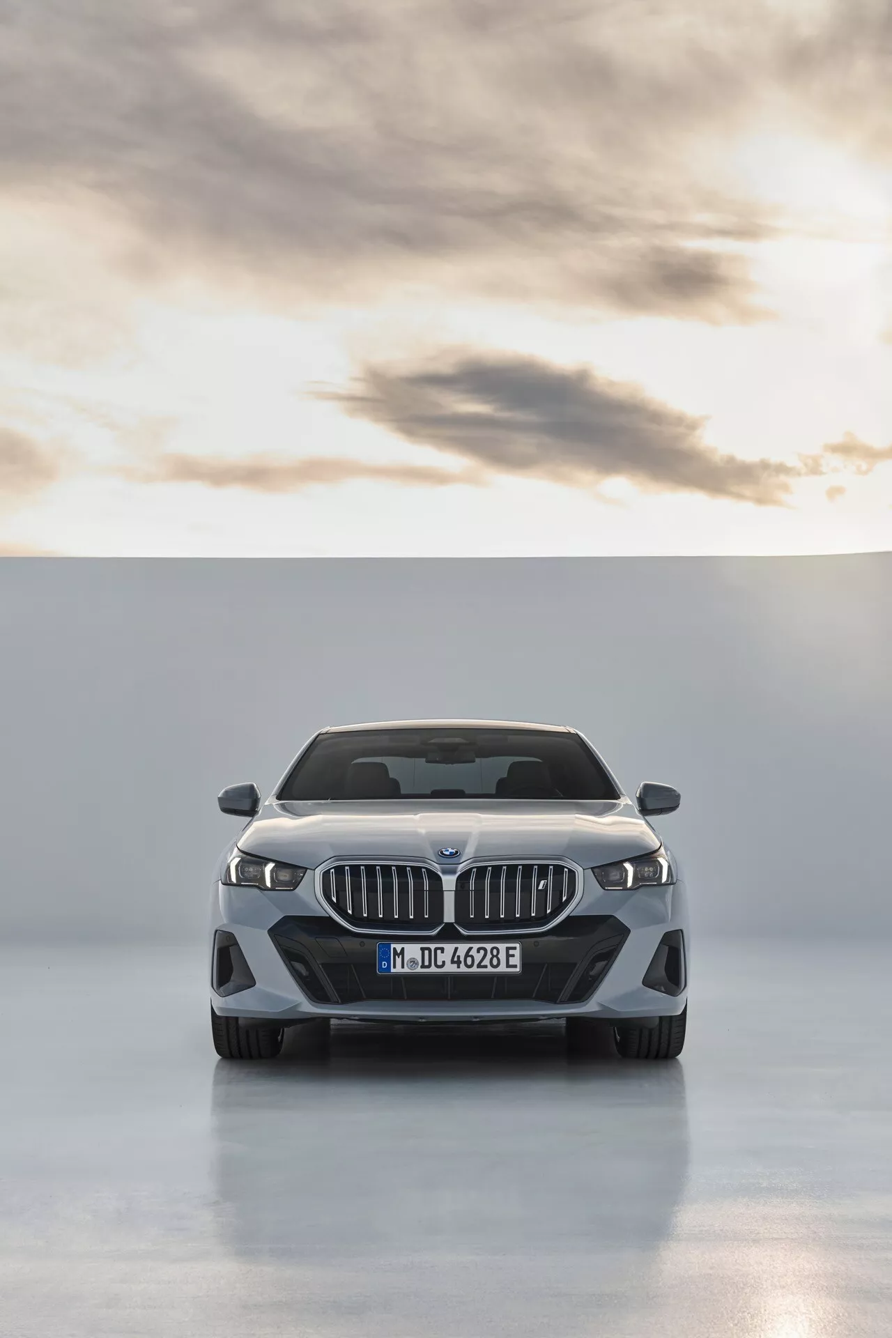 Čelný pohľad na BMW radu 5 (G60-G61) 2023 predstavujúci dvojité obličkovité mriežky, LED svetlomety s dennými svieteniami, kontúrové línie kapoty, emblém výrobcu, predný nárazník orientovaný na výkon s veľkými vzduchovými vstupmi, možné integrované senzory pre asistenčné systémy vodiča, a leštený povrch proti čistému štúdiovému pozadiu