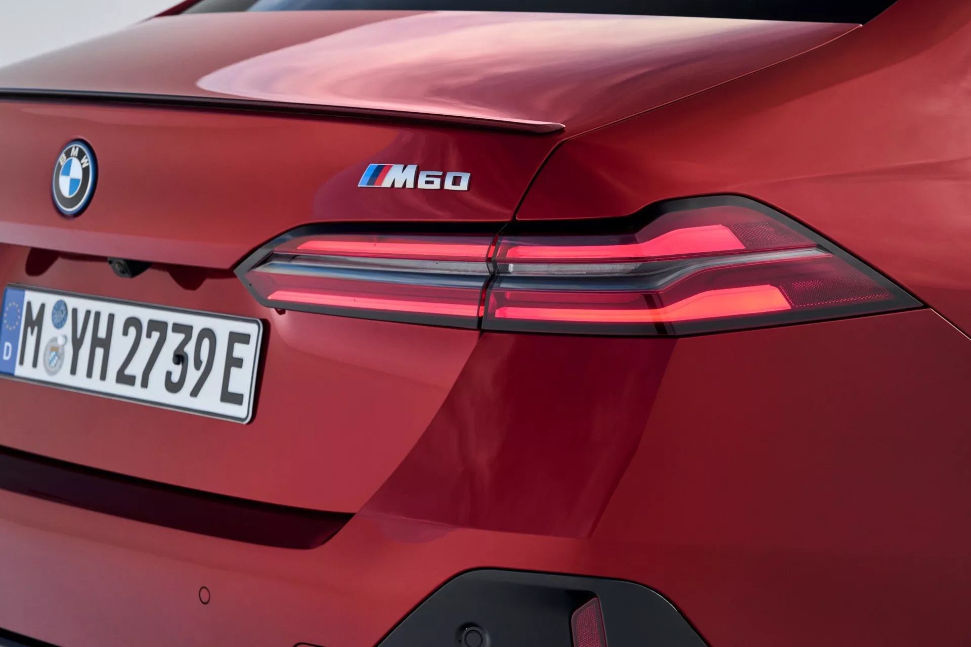 Detailný pohľad na zadnú časť BMW série 5 iM60 z roku 2023, zvýrazňujúci LED zadné svetlá, označenie iPerformance, európsku poznávaciu značku, vysoko lesklý burgundský lak a výrazné dizajnové prvky