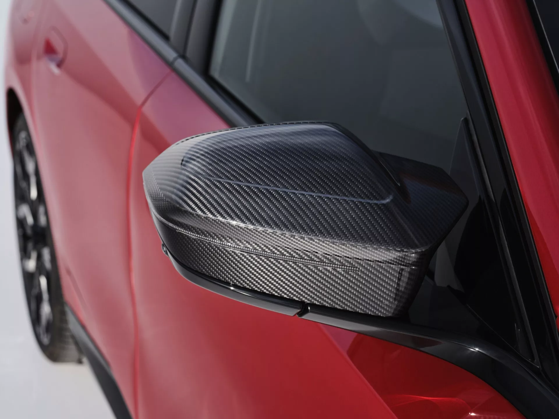 Detailný záber na bočné zrkadlo BMW radu 5 (G60-G61) 2023 s puzdrom z uhlíkových vlákien vo tmavočervenej farbe, zdôrazňujúci aerodynamický dizajn a technológiu materiálov.