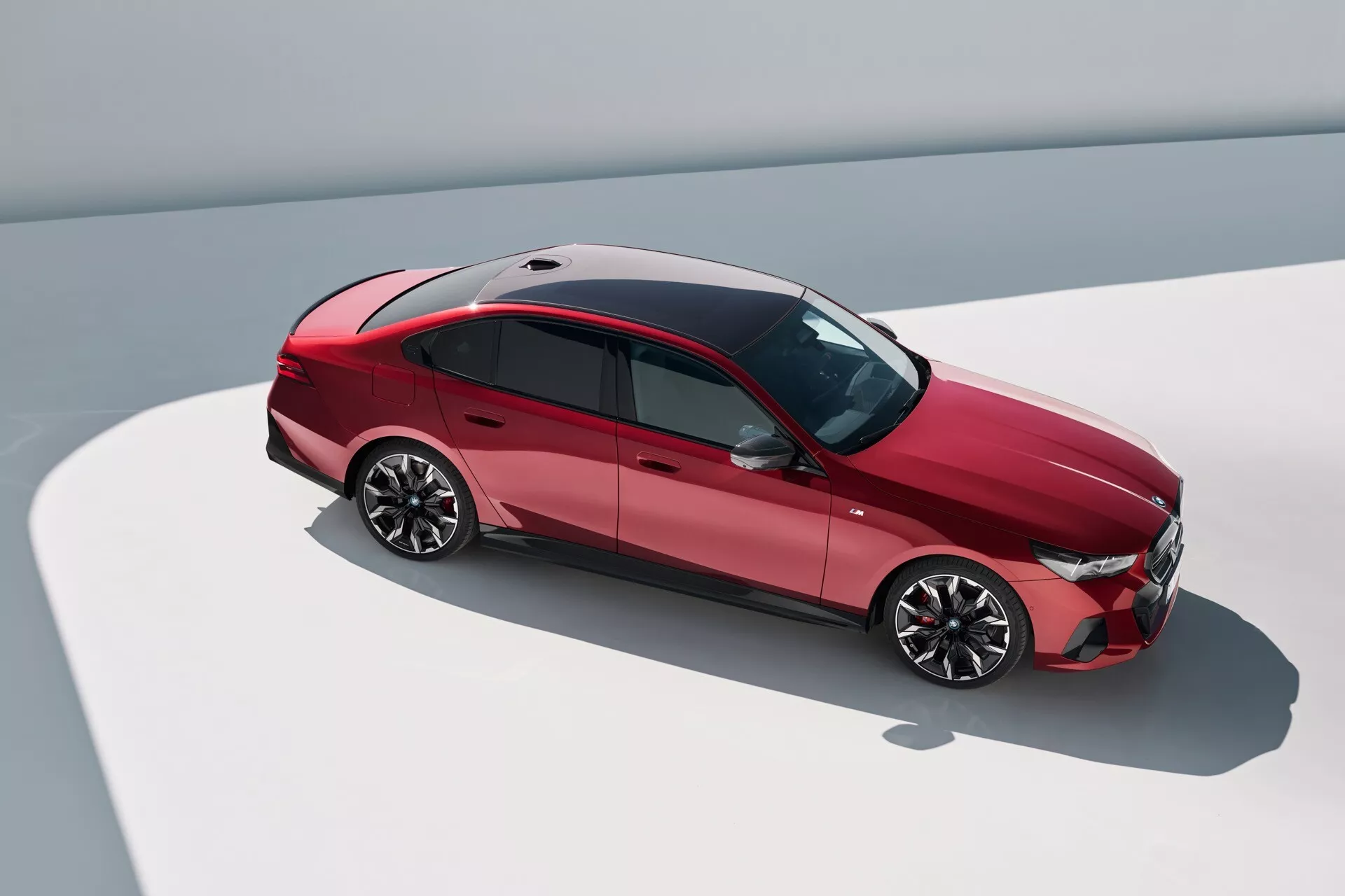 Pohľad zhora pod uhlom na BMW radu 5 z roku 2023 (G60-G61), ukazujúci horný a bočný profil, s aerodynamickým dizajnom, lesklými zliatinovými kolesami, strešným oknom a pokročilou svetelnou technológiou.