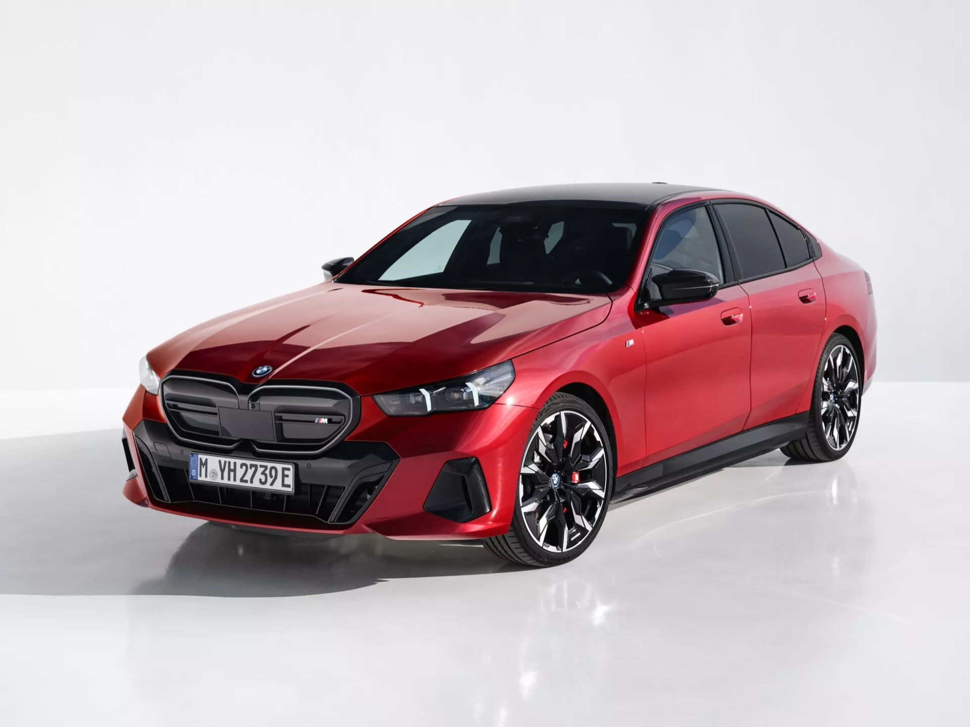 Červený štvordverový sedan BMW radu 5 (G60-G61) z roku 2023 z uhla troch štvrtín zpredu, ktorý zobrazuje dizajn mriežky, štíhle svetlomety a sochársky bočný profil na odrazovej ploche s bielym pozadím