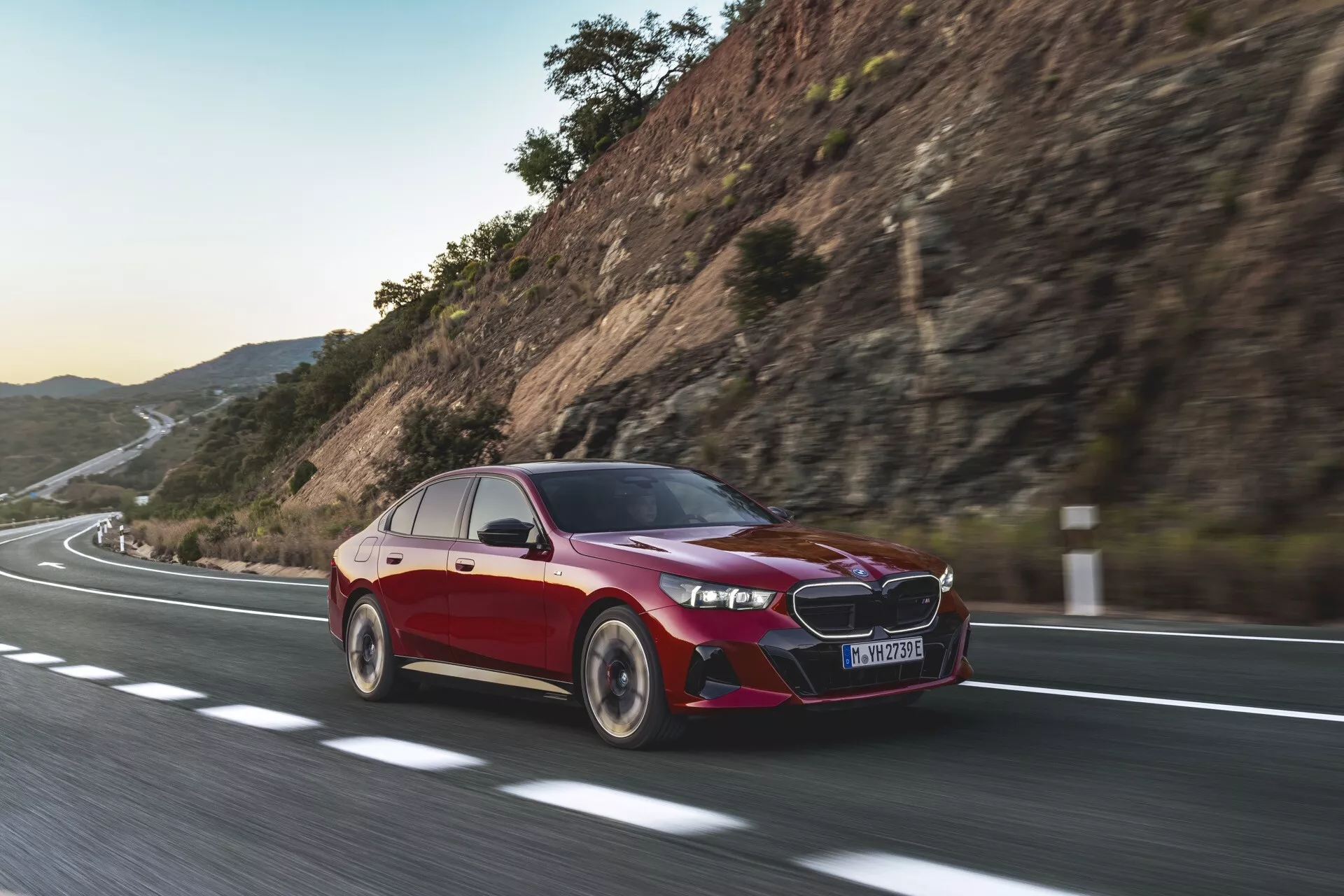 Sedan BMW radu 5 (G60-G61) 2023 v pohybe, ukazujúci dynamické jazdné schopnosti so zameraním na pokročilé automobilové technológie, LED svetlomety a aerodynamický dizajn pod mäkkým slnečným svitom.