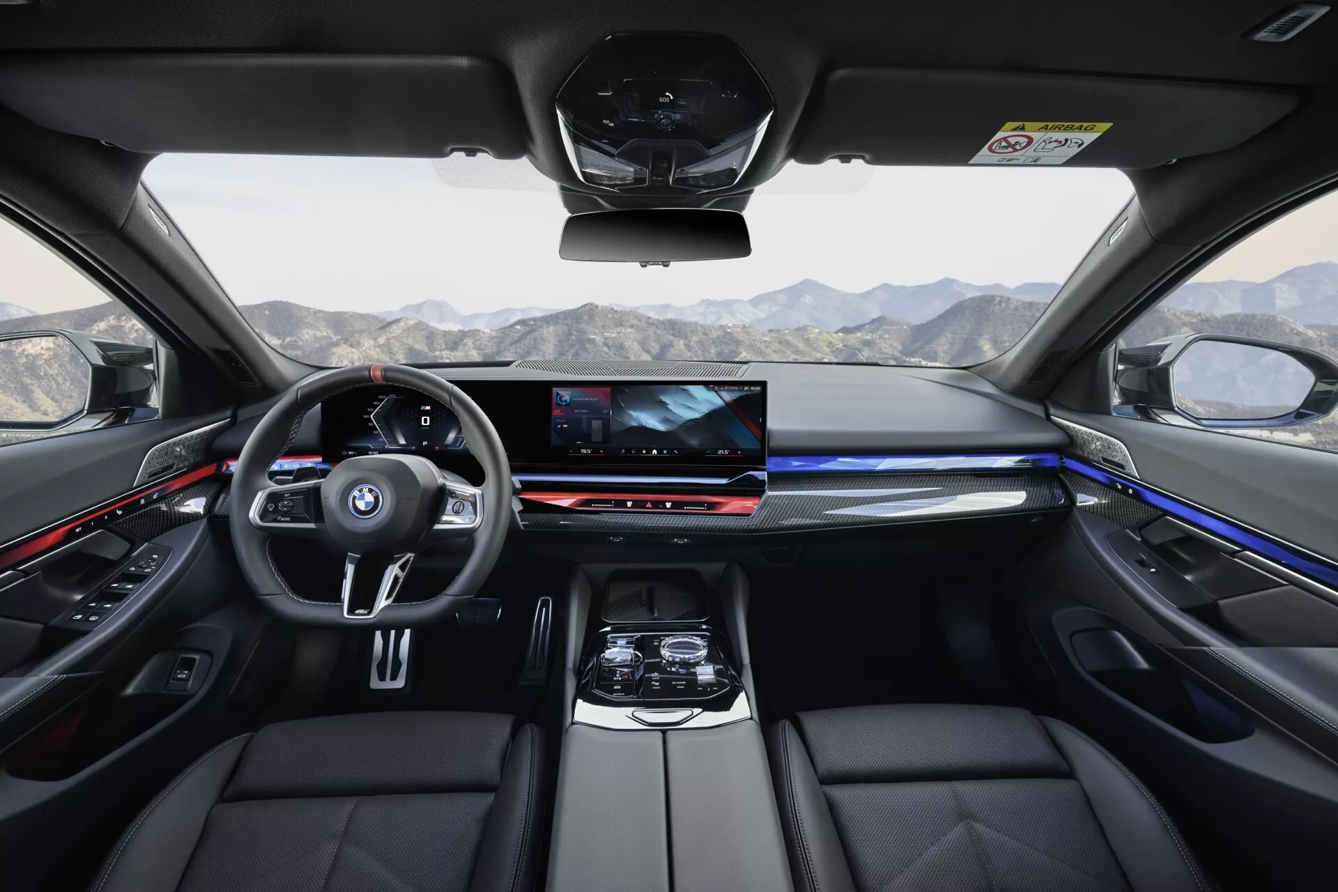 Interiérový pohľad na BMW radu 5 z roku 2023 (G60-G61) zobrazujúci palubnú dosku, predné sedadlá a technologické funkcie z pohľadu zadného sedadla