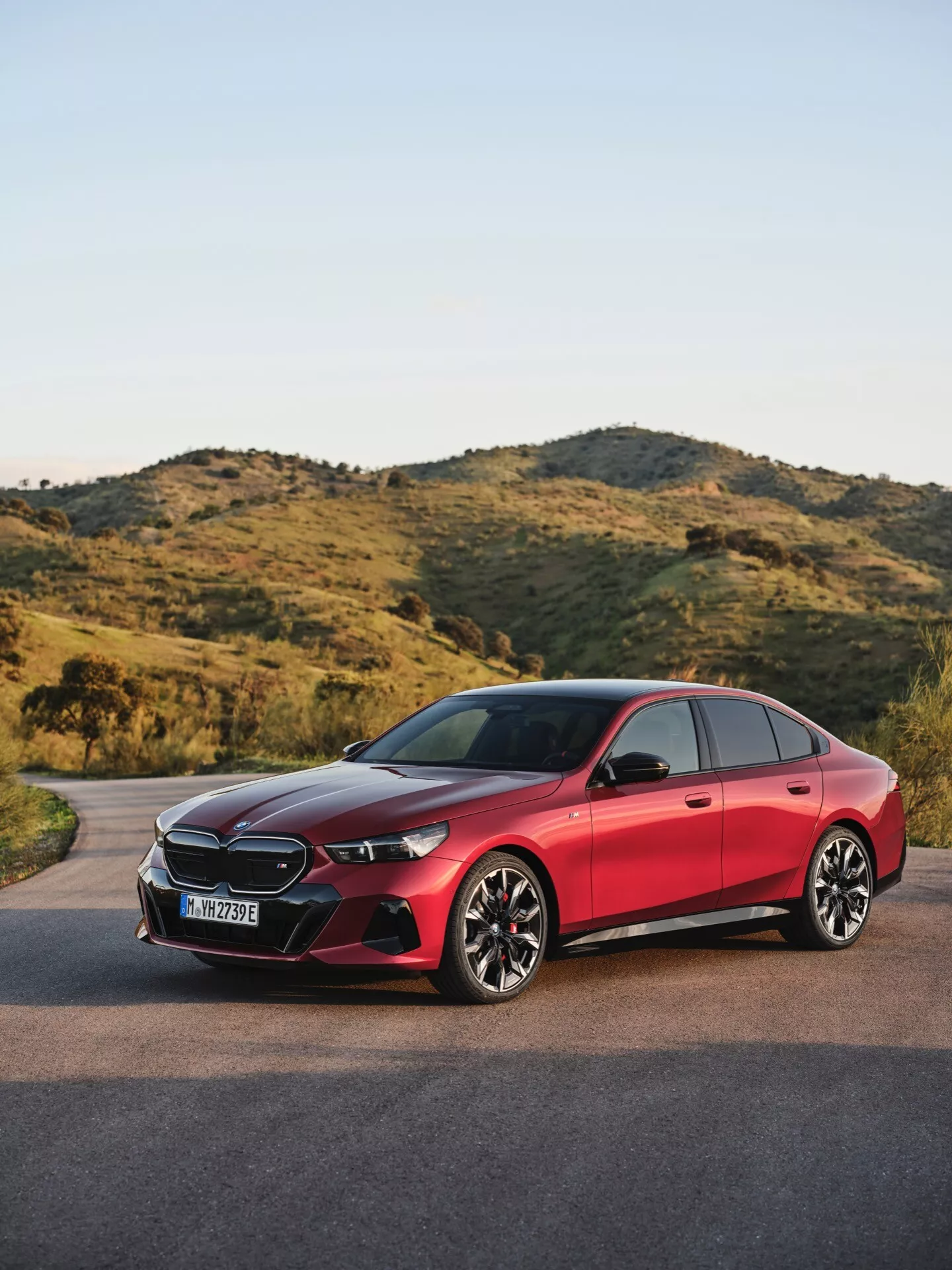 BMW radu 5 2023 (G60-G61) vo vzhľade tri štvrtiny spredu na asfaltovej ceste s prírodnou, kopcovitou krajinou na pozadí, predvádzajúci LED svetlomety, senzory integrované do mriežky, nasávacie otvory, športové disky z ľahkých zliatin, systém bezkľúčového vstupu a vysokokvalitný lesklý povrch