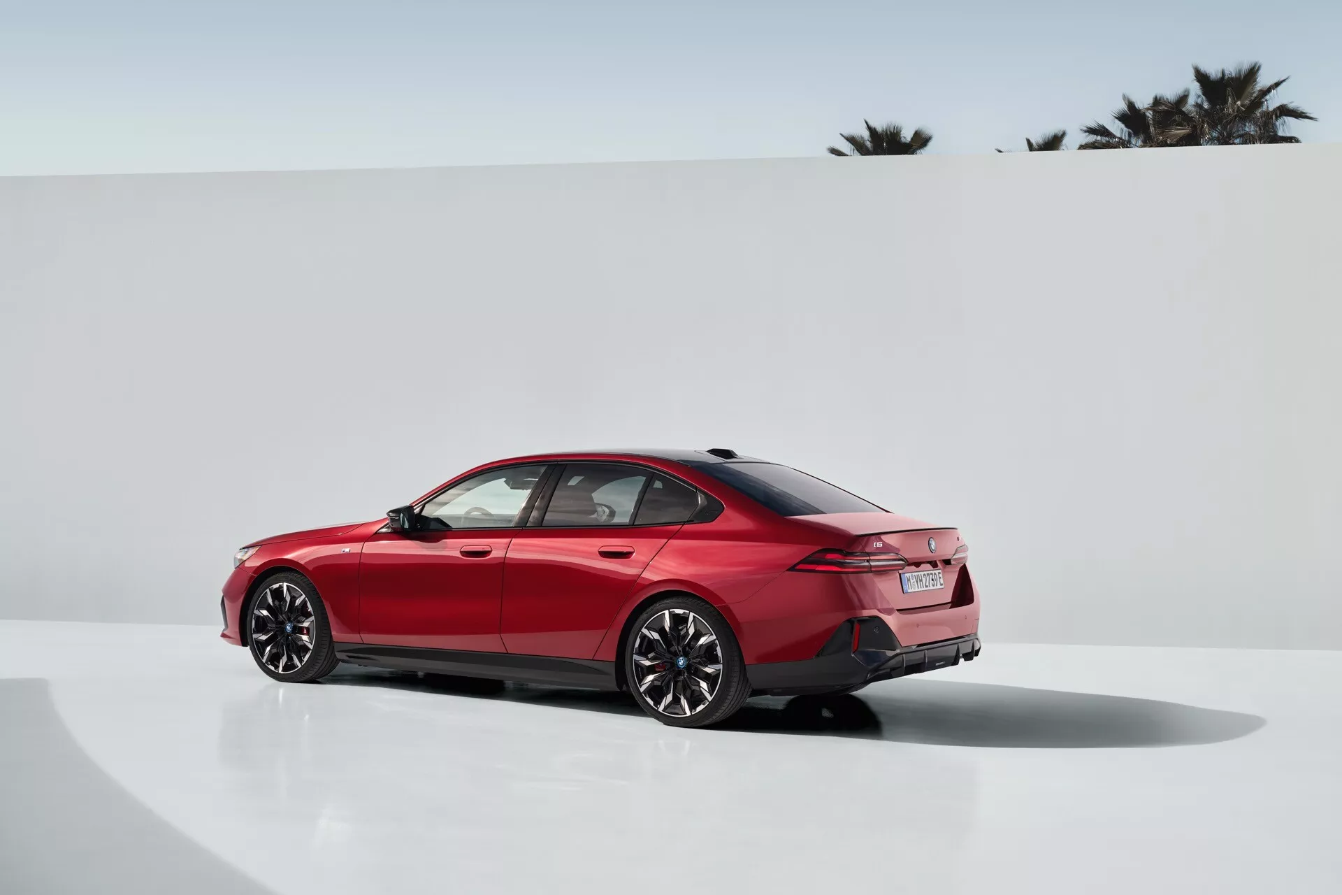 BMW radu 5 z roku 2023 (G60-G61) vo výraznej červenej farbe, ktoré prezentuje svoj sofistikovaný dizajn z trojštvrťového zadného uhla, s vysokolesklým povrchom, športovými viacramennými zliatinovými kolesami a pokročilým LED zadným osvetlením na pozadí minimalistického fotostudia