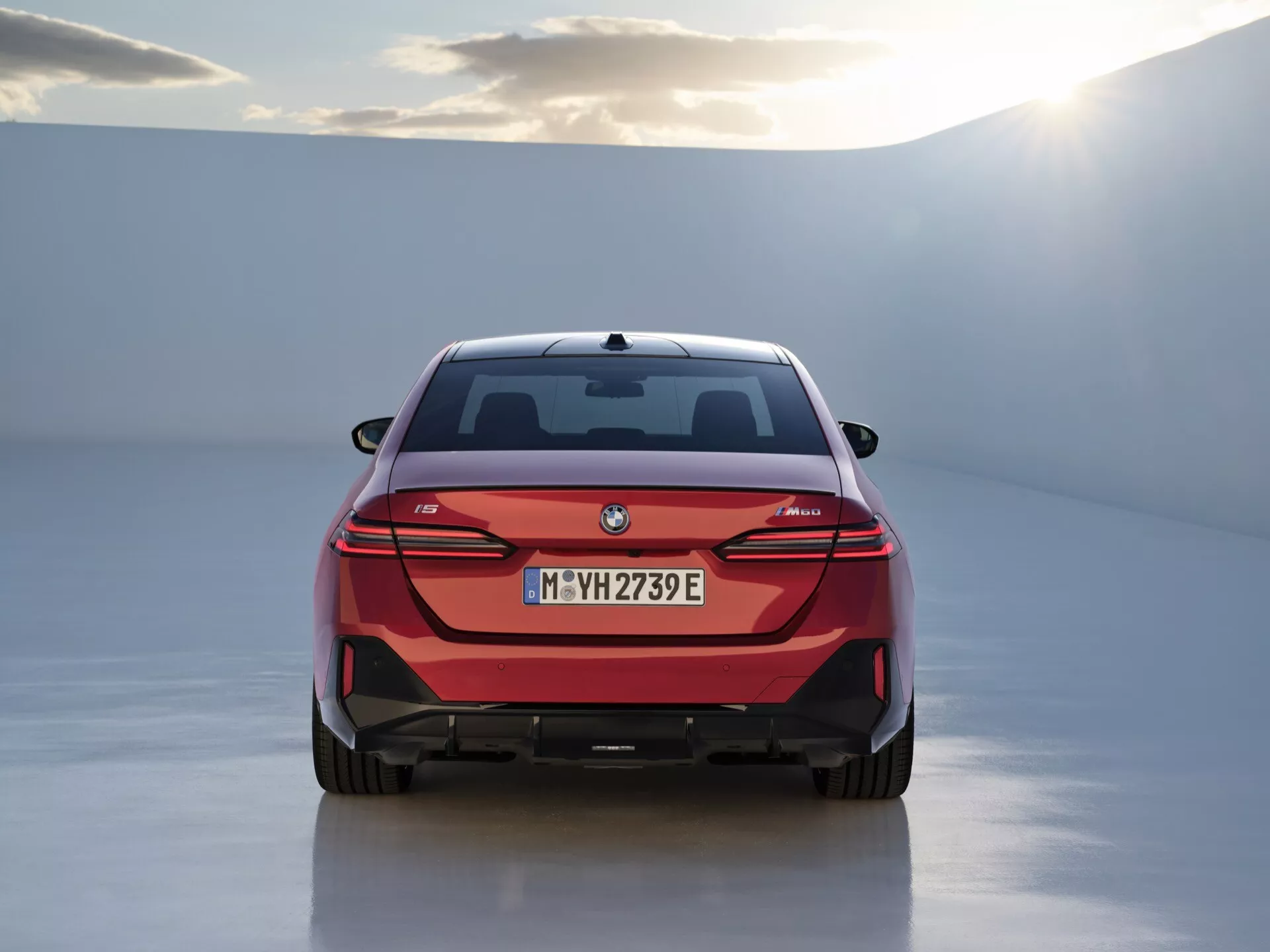 Zadný pohľad na elektrické auto BMW i4 s LED zadnými svetlami, odznakom technológie eDrive a nárazníkom v štýle difúzoru, predstavený v štúdiu s bielou odrazivou podlahou a mäkkým osvetlením.