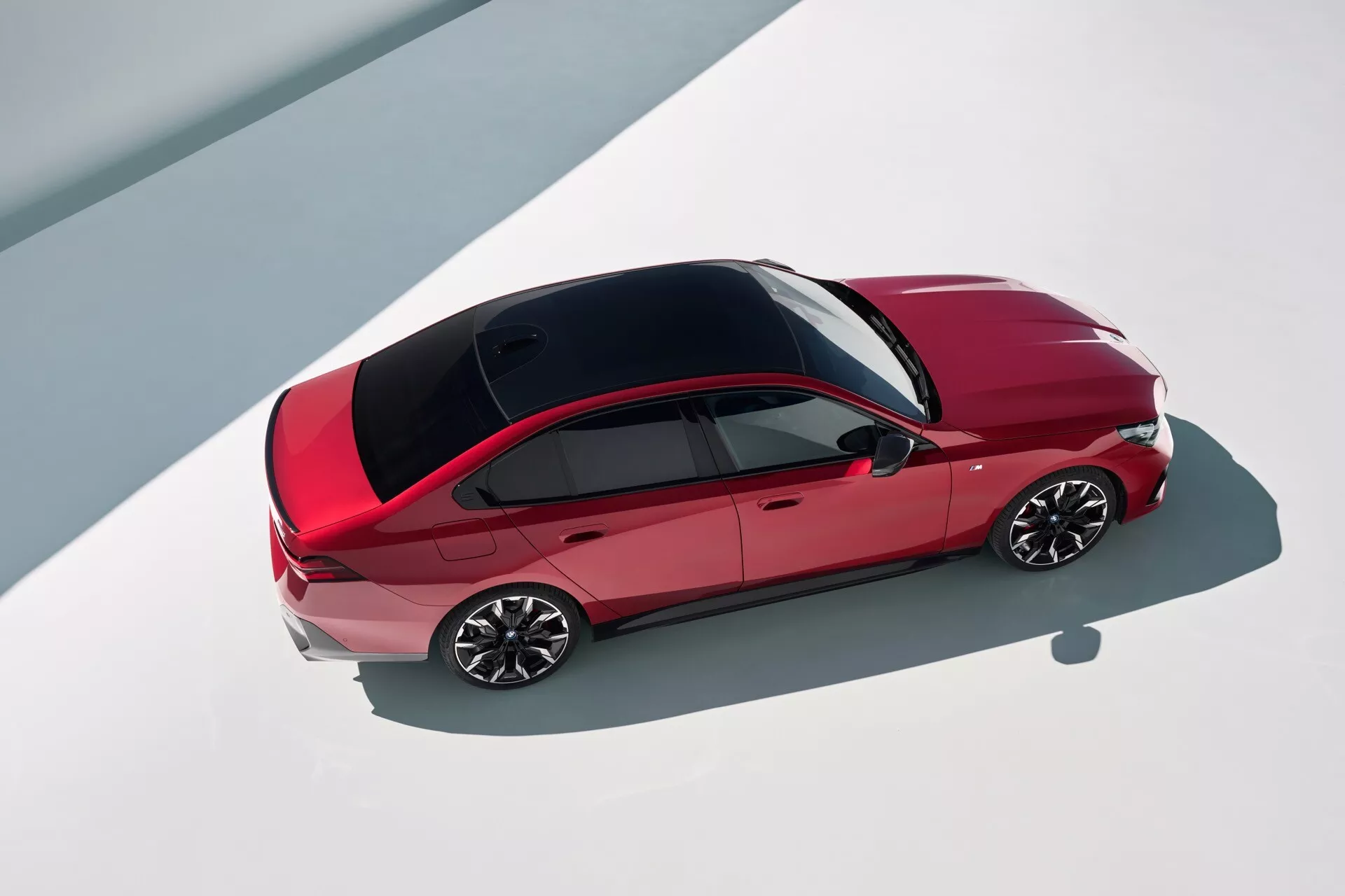 Sedan BMW radu 5 2023 (G60-G61) v červenej farbe so štíhlym dizajnom s kontrastnou čiernou strechou a viacramennými kolesami z pohľadu zhora, zdôrazňujúci kontúry vozidla zhora a dizajnovú estetiku