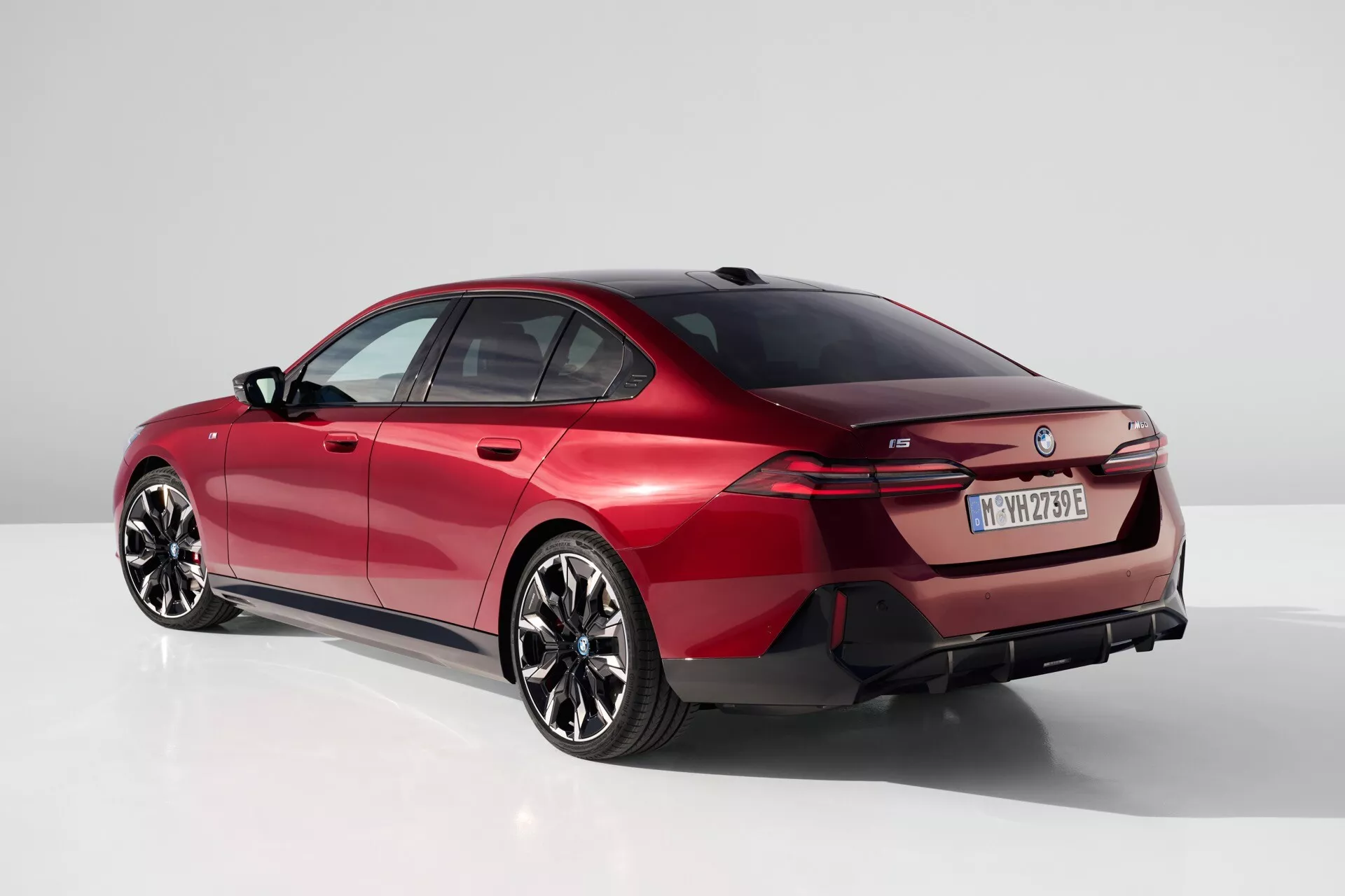 Moderné sedan BMW radu 5 (G60-G61) z roku 2023 v štúdiovom nastavení, záber z trojštvrťového zadného uhla zdôrazňujúci elegantnú líniu strechy, výrazné zadné svetlá a športový aerodynamický profil vo výraznej červenej