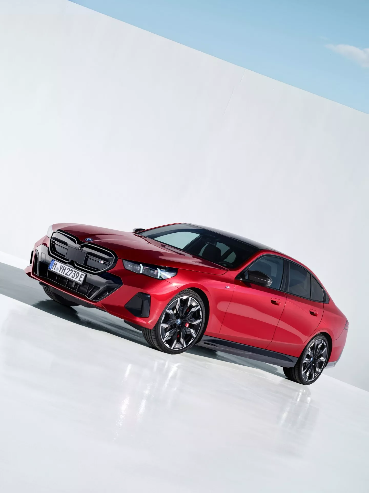 BMW radu 5 z roku 2023 (G60-G61) vo výraznej červenej farbe predstavujúce športový dizajn s výraznou mriežkou chladiča, LED svetlometmi, tvarovanými dverovými panelmi a viacramennými zliatinovými kolesami v jasnom štúdiu