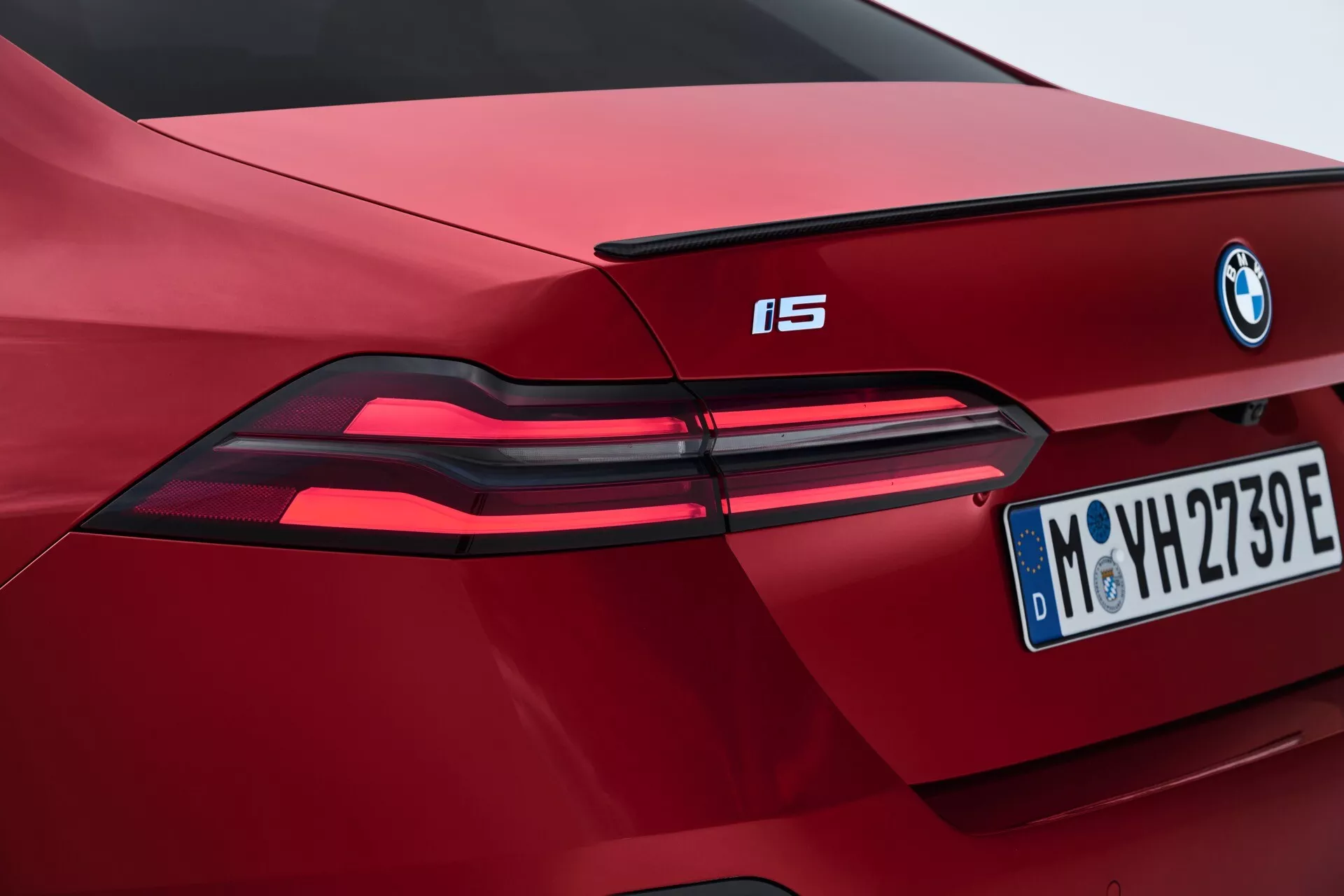 Detailný pohľad na čiastočný zadný pohľad červeného BMW i5 z roku 2023, ukazujúci moderné LED zadné svetlá, výrazné logo BMW a európsku poznávaciu značku z Mníchova, zdôrazňujúci rysy elektrického vozidla