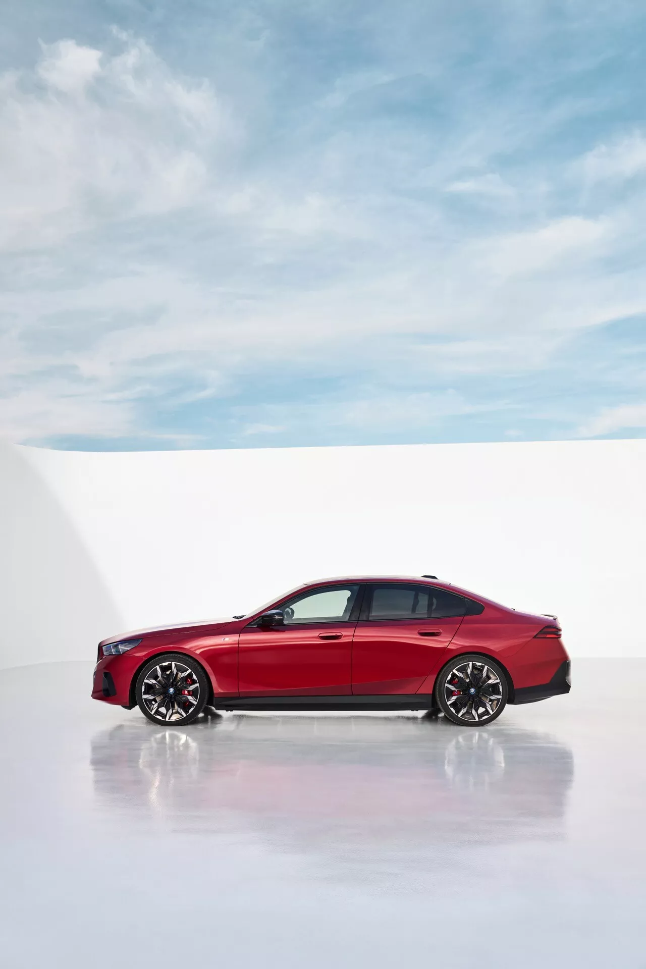 Moderný bočný pohľad na BMW radu 5 (G60-G61) 2023 vo výraznej červenej, zdôrazňujúci štíhle dizajnové línie a športové zliatinové kolesá na bielom pozadí profesionálneho štúdia