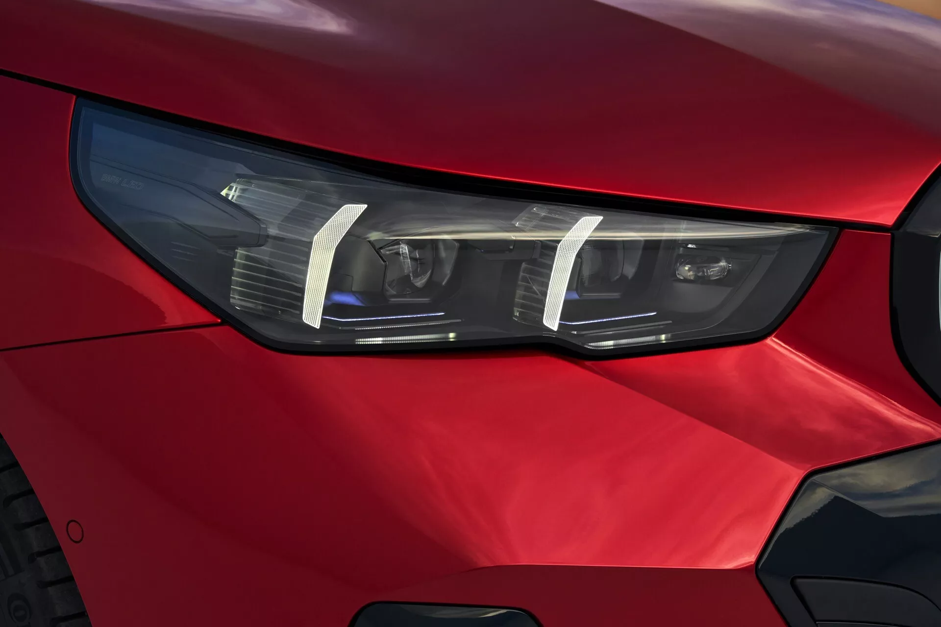 Detailný pohľad na predné svetlo na strane vodiča modelu BMW radu 5 (G60-G61) 2023 s technológiou LED alebo HID, štíhlym uhlovým dizajnom a živou červenou farbou, ktorý zdôrazňuje pokrokový automobilový dizajn a prémiovú estetiku.