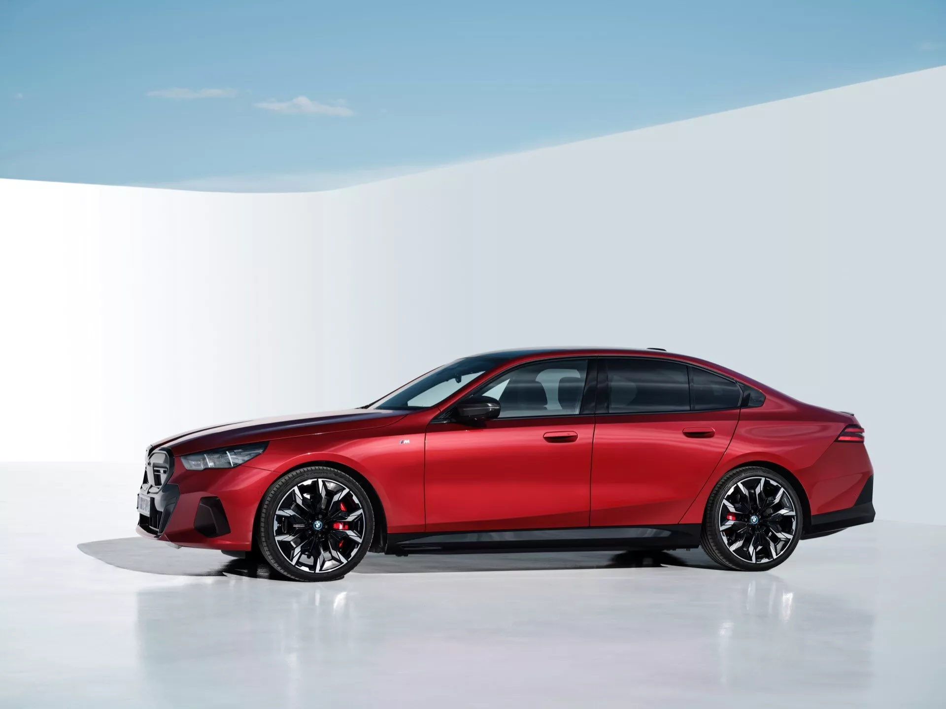 Moderný červený sedan BMW radu 5 (G60-G61) roku 2023 v profile, zobrazujúci prednú mriežku a súbor svetlometov na bielom štúdiovom pozadí, zdôrazňujúci dizajnové a technologické prvky ako LED osvetlenie, športové zliatinové kolesá a pokročilú brzdovú technológiu.