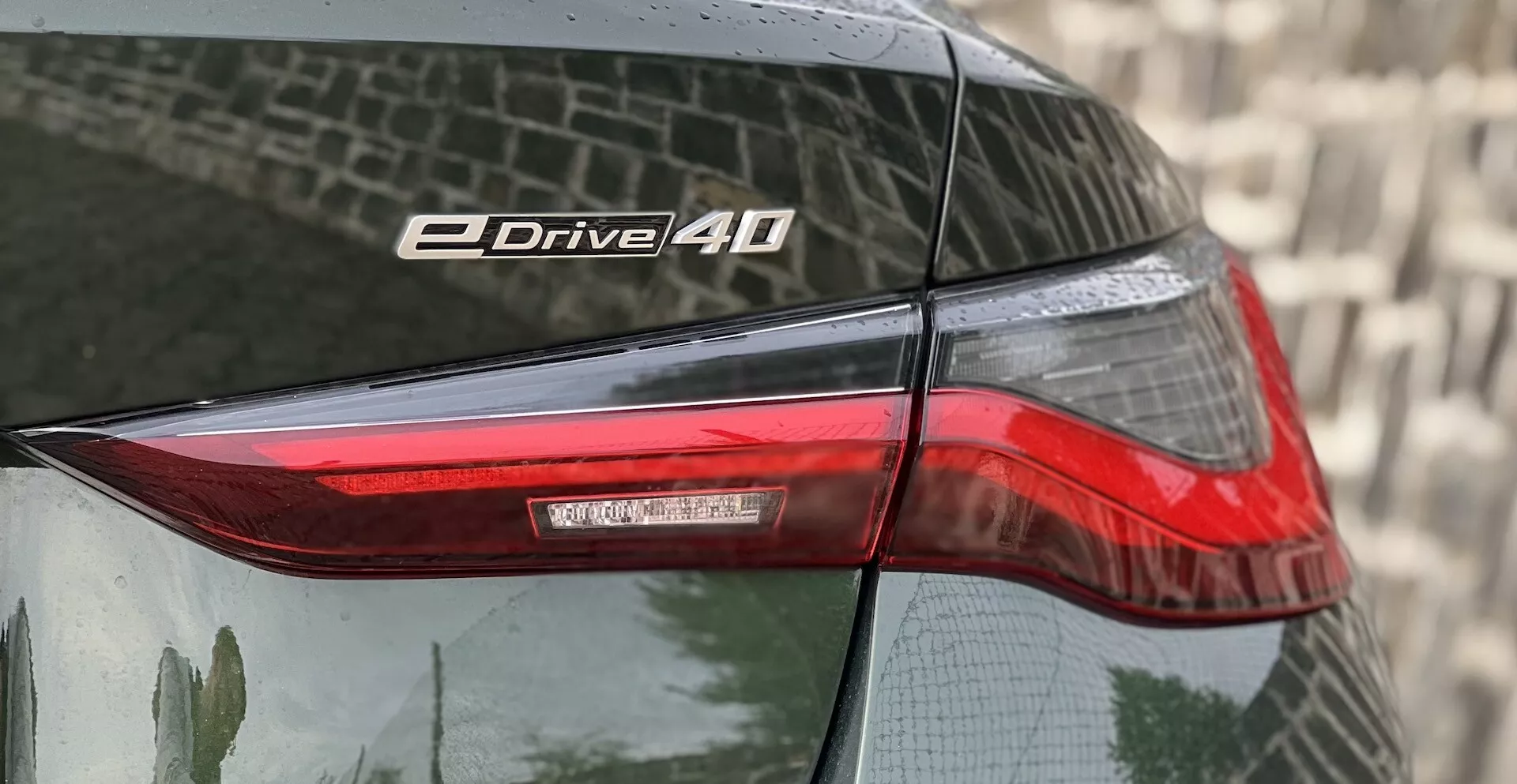 Detailný pohľad na zadný roh BMW i4 2021 so zameraním na zadné svetlo a označenie eDrive 40 s technológiou LED a odrazivým lakom.