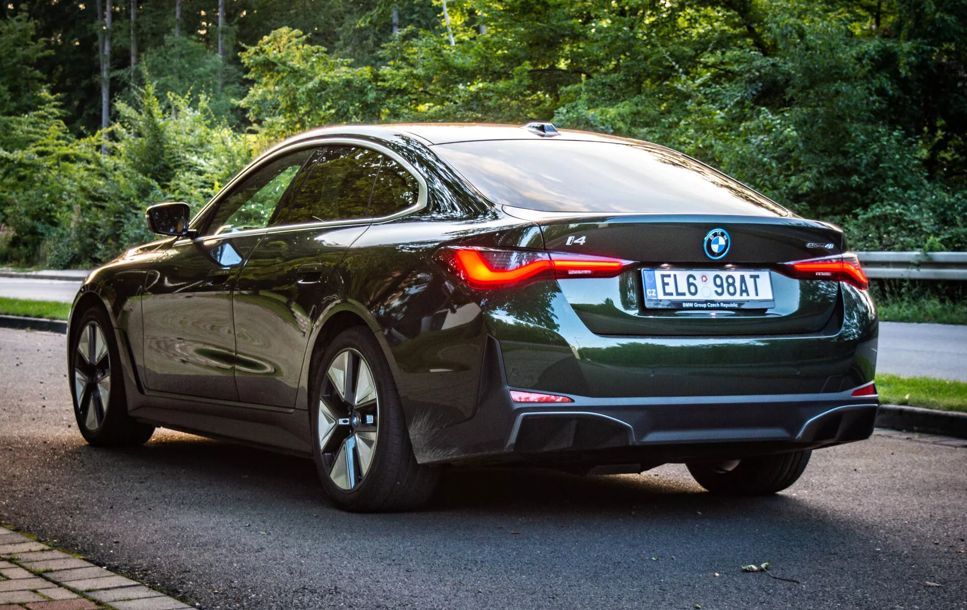 BMW i4 z roku 2021 v elegantnej čiernej farbe, ukazujúce jeho luxusný dizajn a pokročilú technológiu z pohľadu zadnej trojštvrtiny, obsahuje LED zadné svetlá, aerodynamický profil a zliatinové kolesá, zaparkované v prírodnom prostredí.